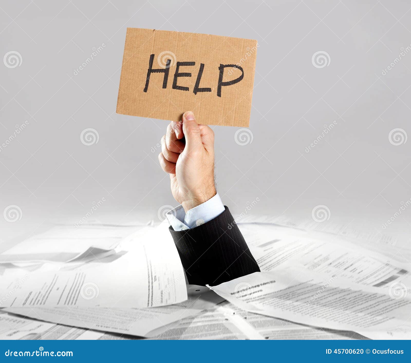 hand of businessman emerging from loaded paperwork desk holding help message