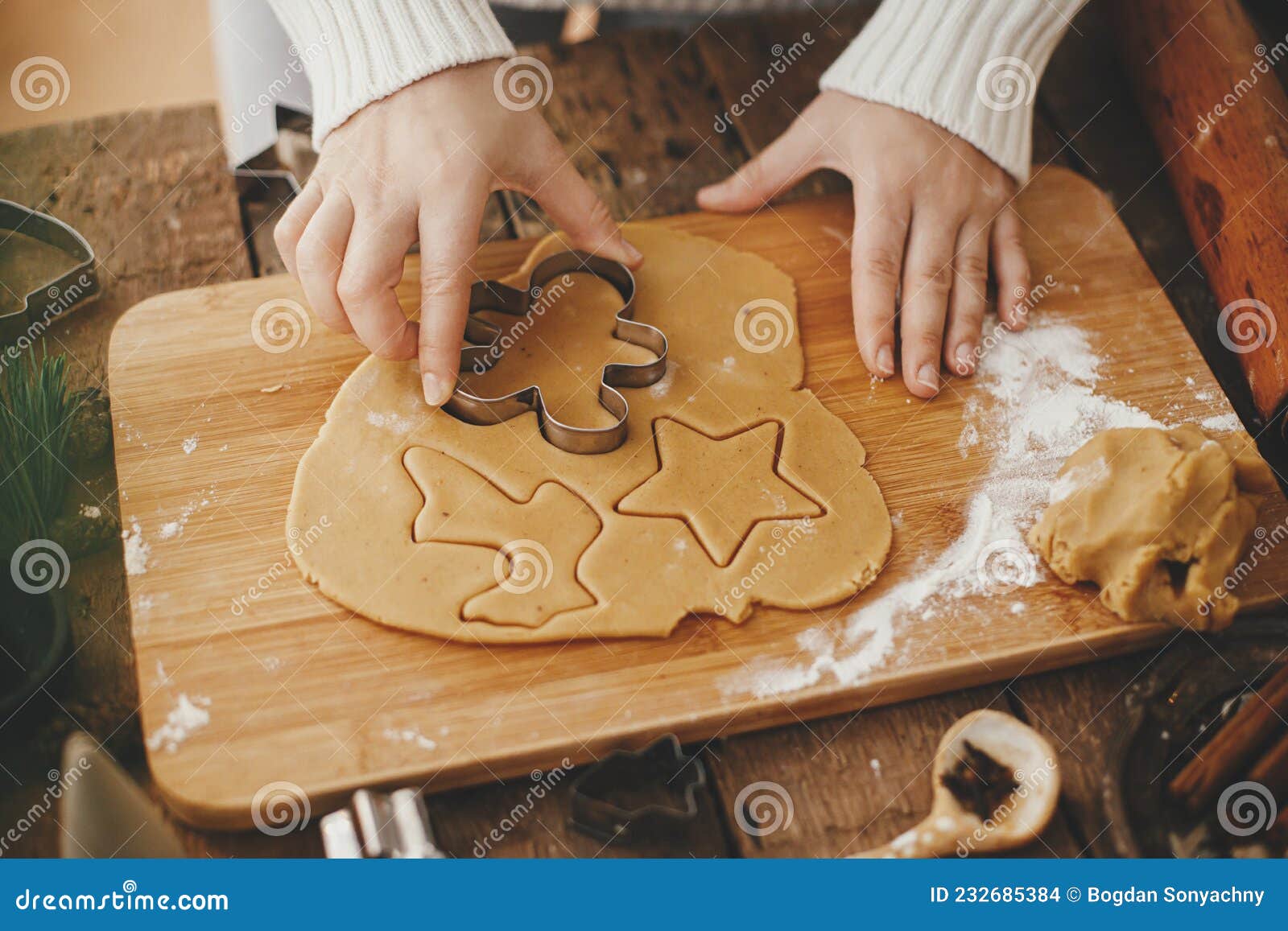 hand cutting gingerbread dough with christmas metal cutters on wooden board. moody image. making traditional christmas gingerbread