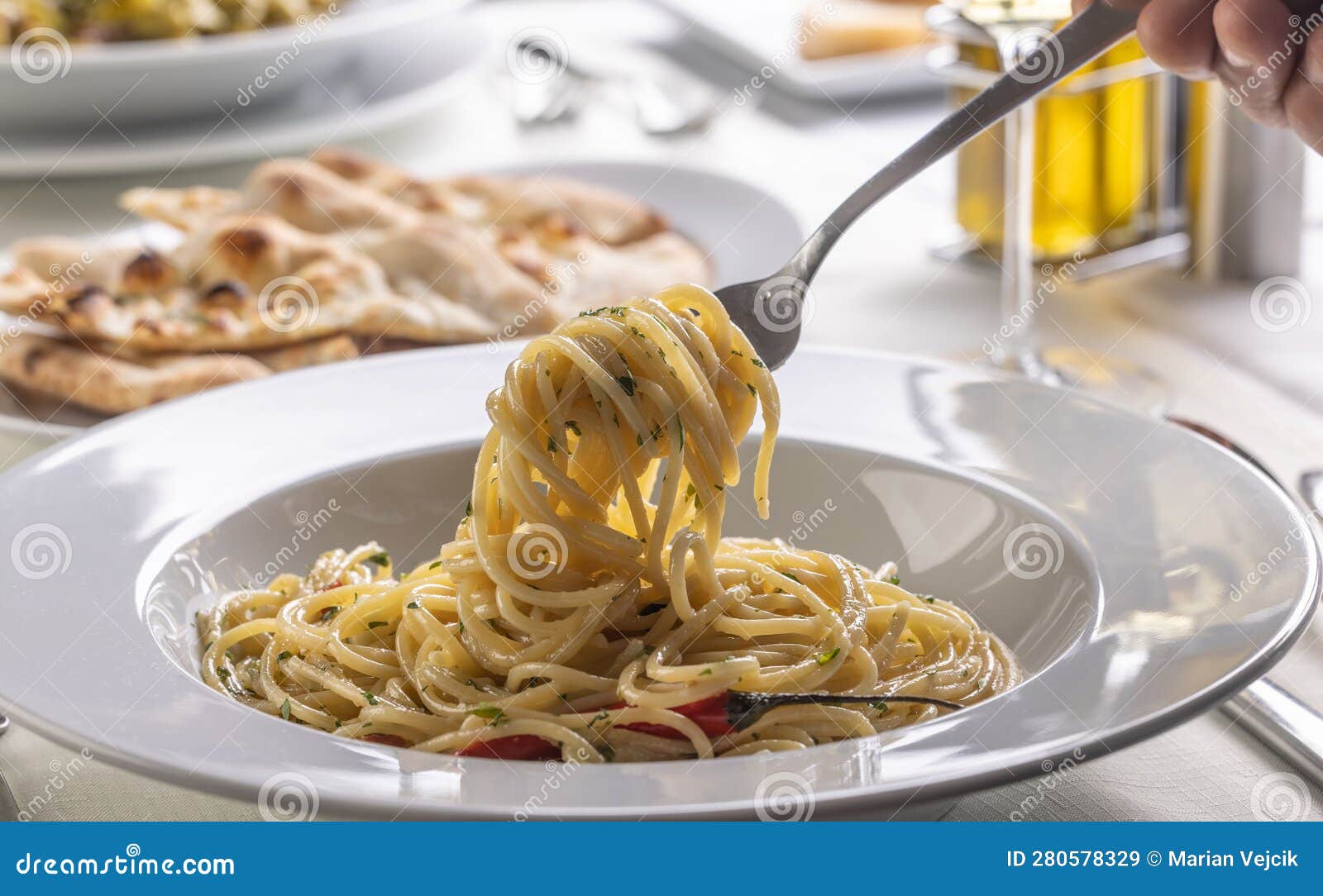 hand with a fork spinning spaghetti aglio e olio peperoncino from a plate in a restaurant