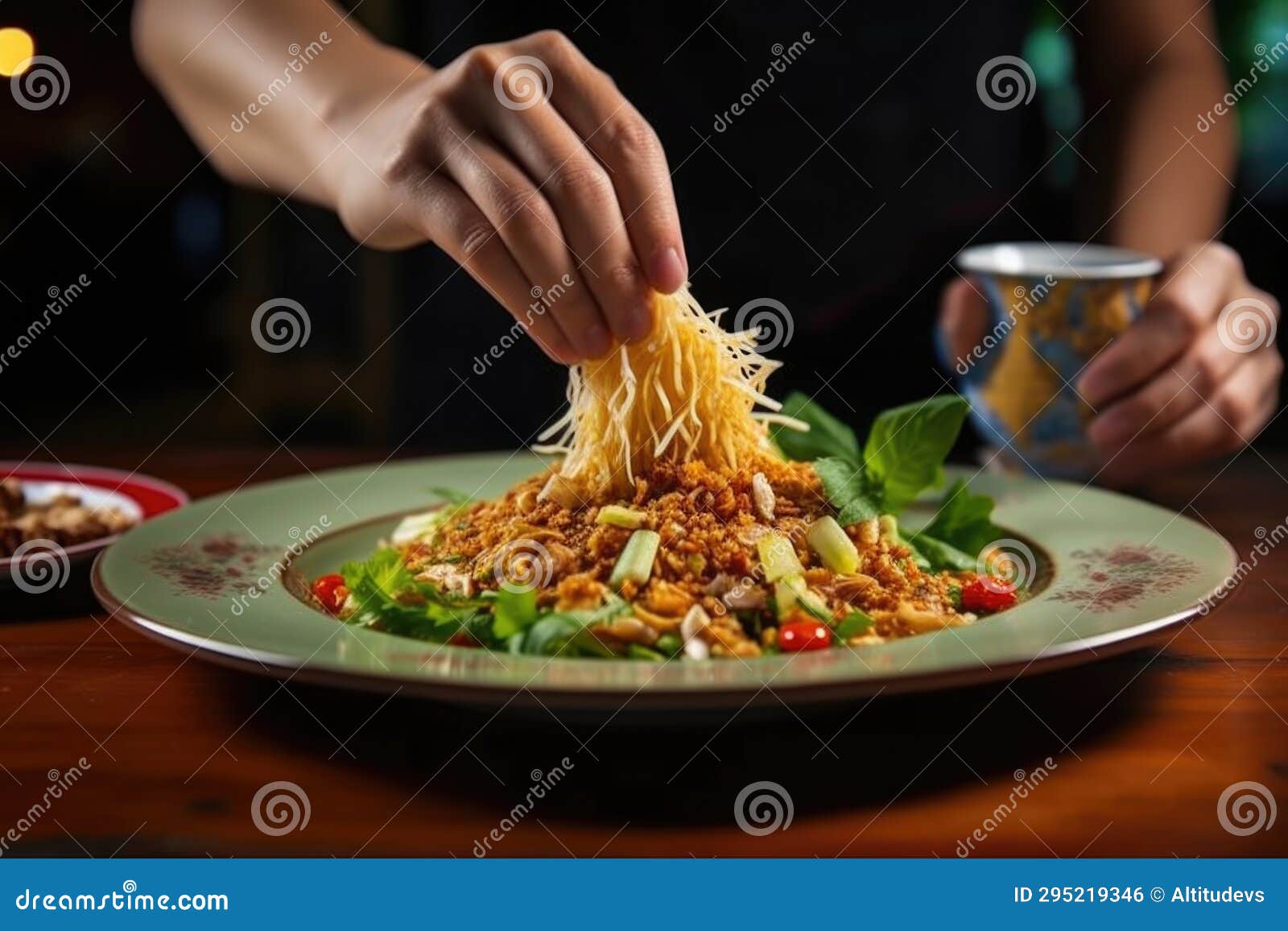 A Hand Garnishing Pad Thai with Crushed Peanuts on a Plate Stock Photo