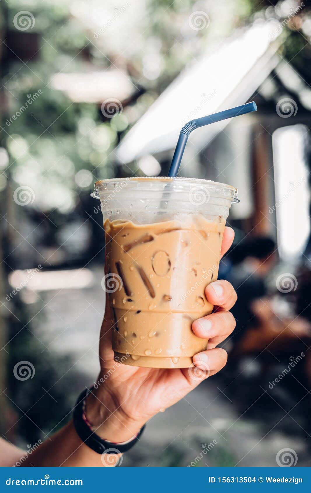 Hand Holding Iced Latte with Straw in Plastic Cup at Garden Blur