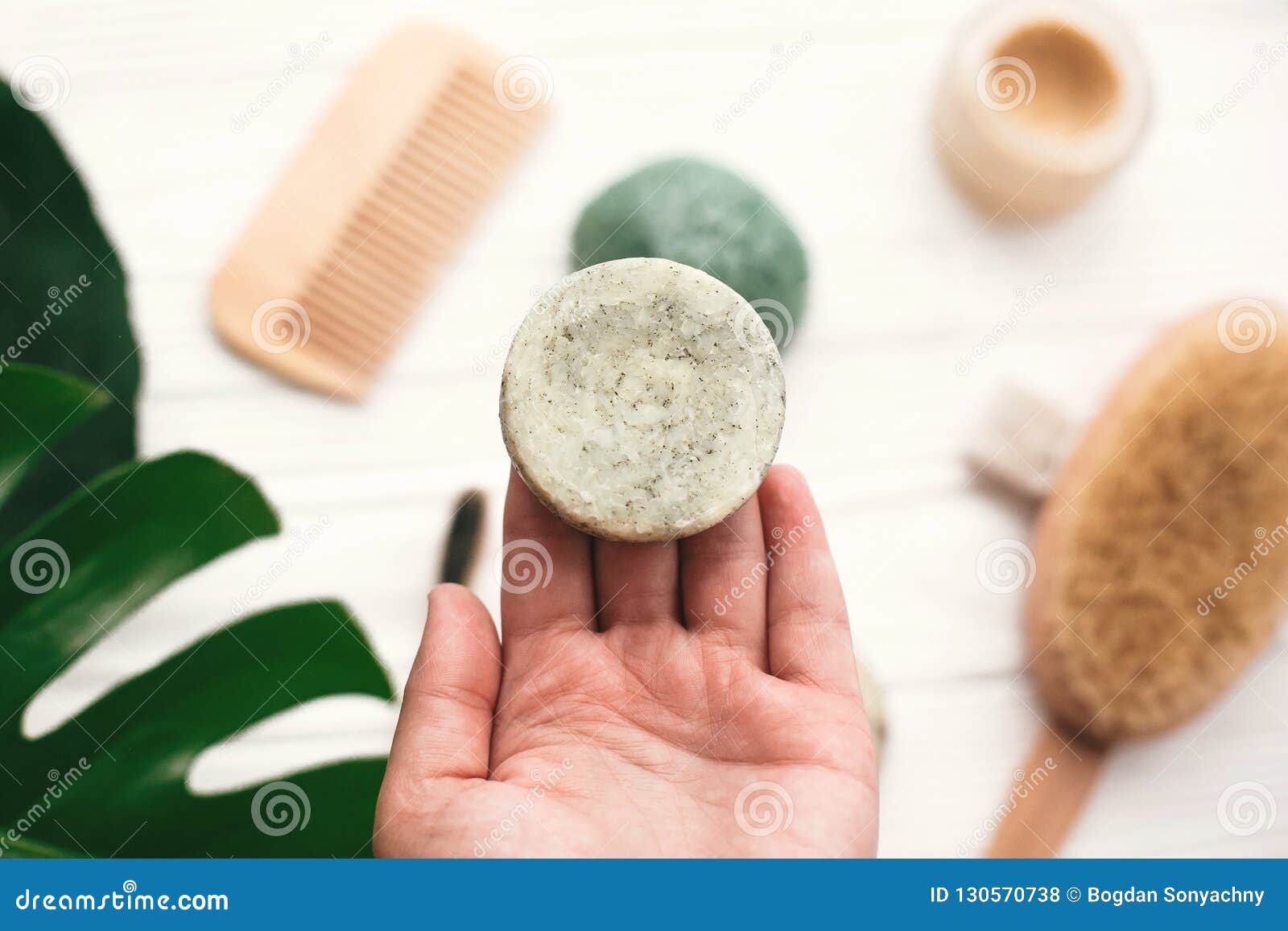 hand holding natural solid shampoo bar on background of bamboo b