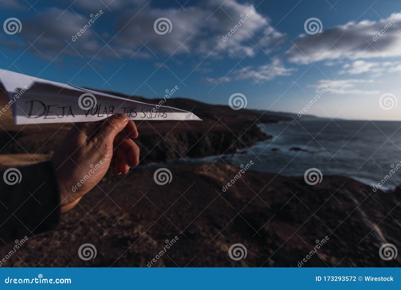 hand holding a paper plane with the words deja volar tus suenos, spanish for let your dreams fly