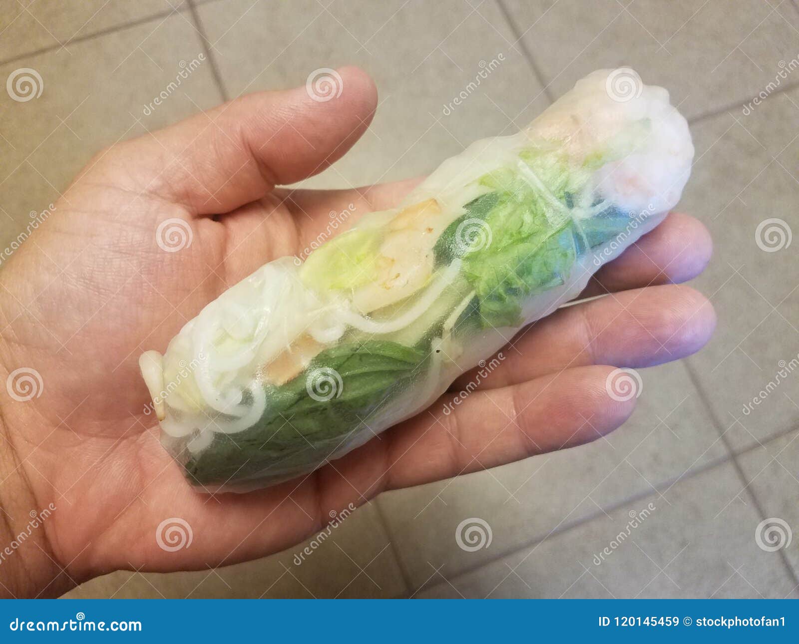 hand holding a shrimp and rice noodle roll over tiled floor