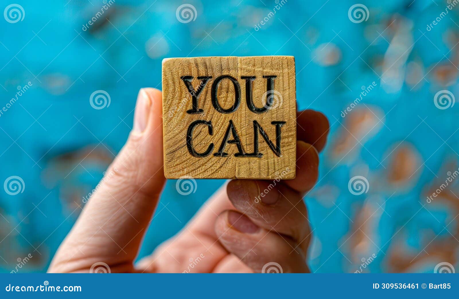 hand holding a wooden block with yes you can inspiring confidence, motivation, and positivity on a bright blue background for