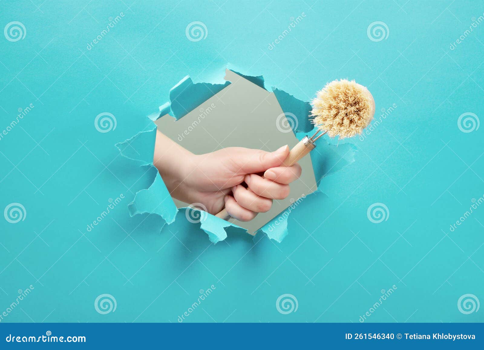 hand holds a dishwashing brush through a paper hole.