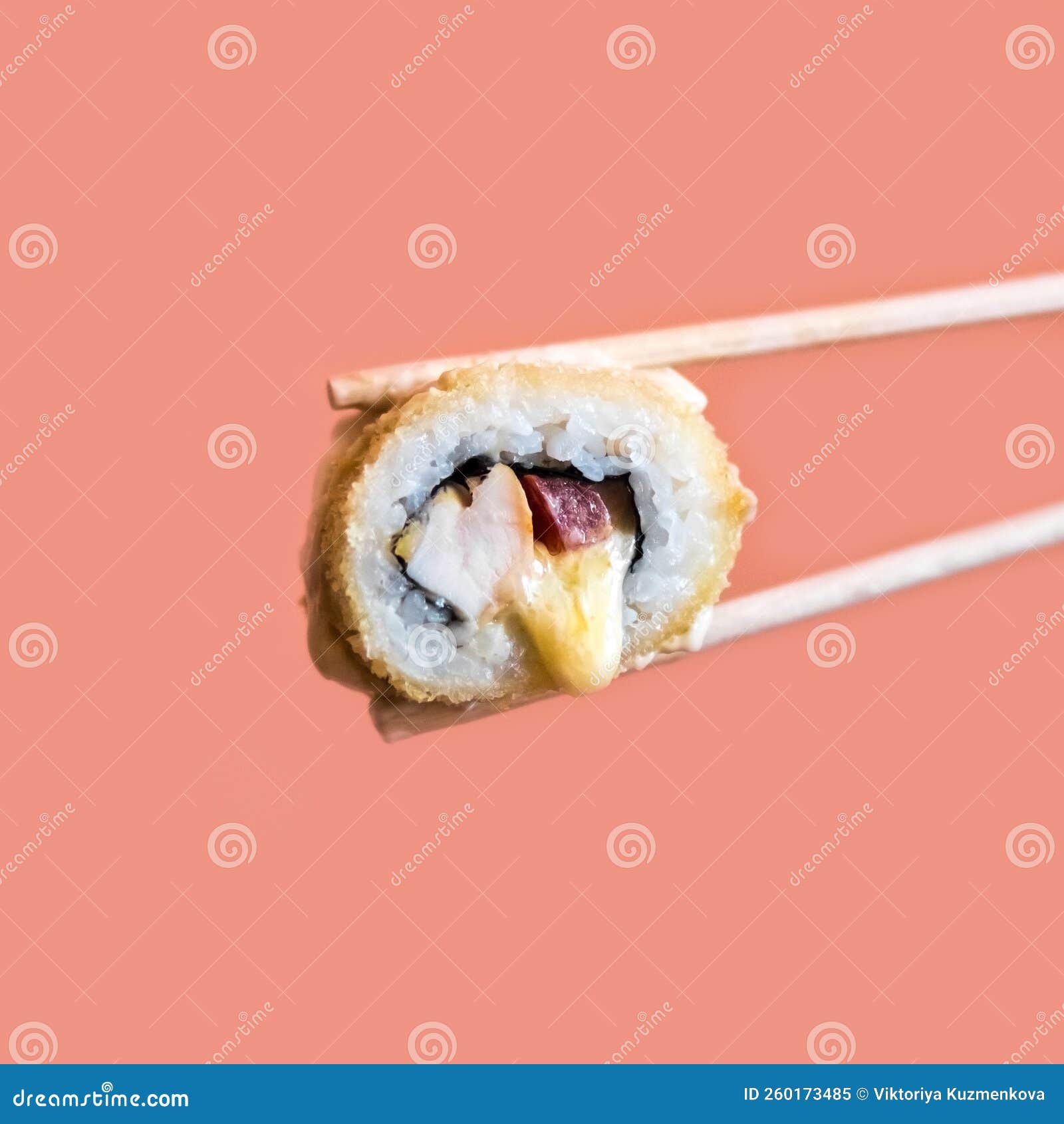 A Hand Holds a Fried Sushi Roll with Cheese with Wooden Sticks Stock