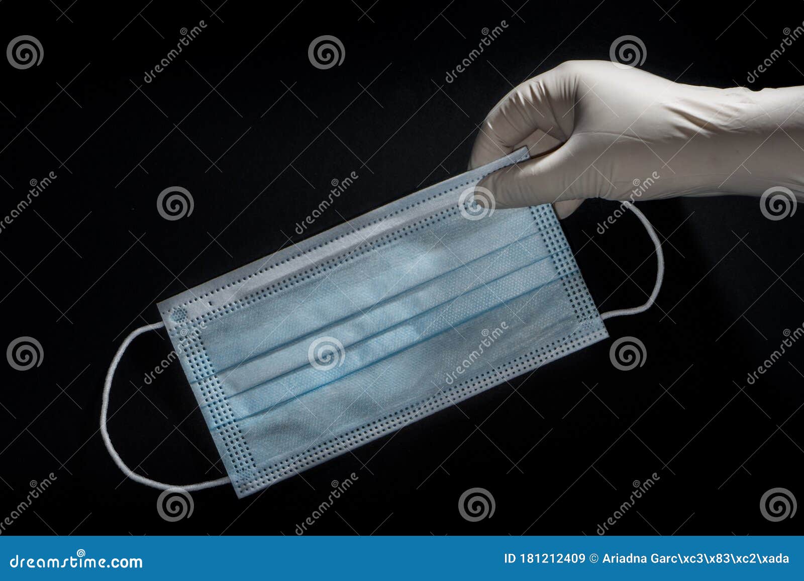 a hand with a latex glove picking up a face mask for virus protection on black background