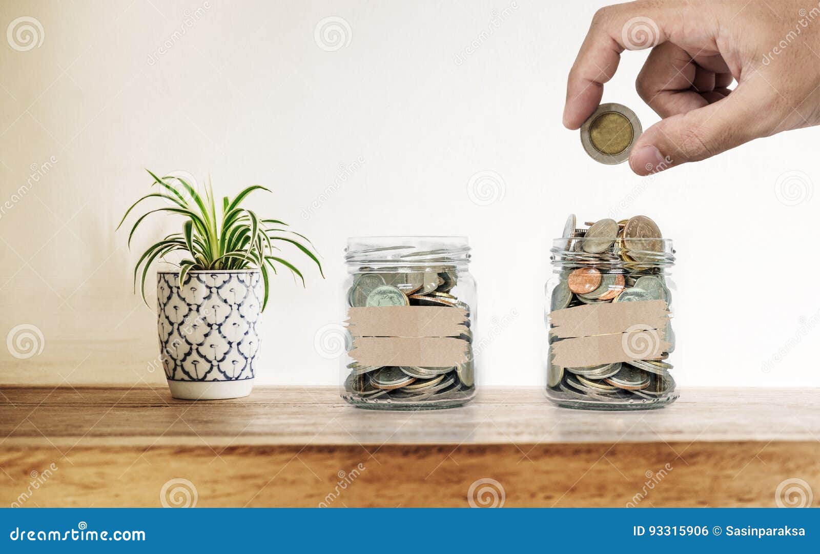 hand putting coin in glass bottles, with decoration plant on wooden desk, saving money , investment and economize 