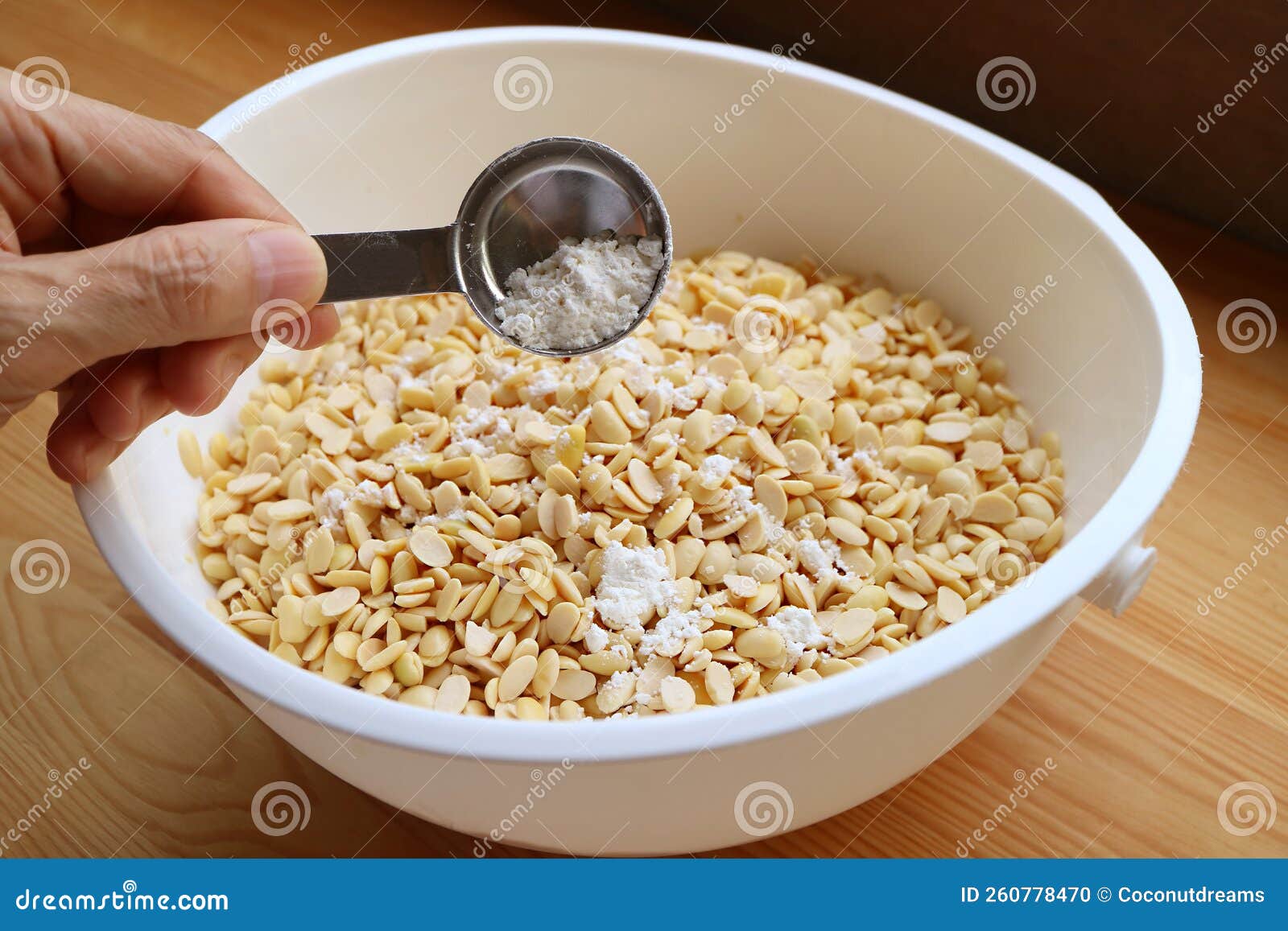 Hand Putting a Spoon of Tempeh Starter into Boiled Soybeans Bowl before