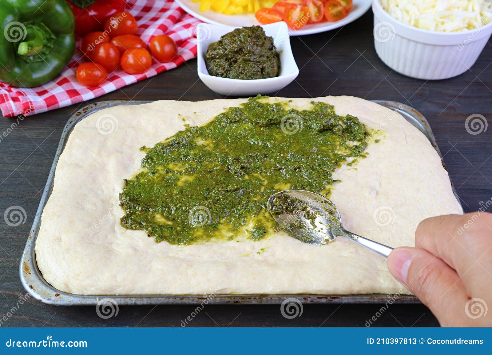 hand spreading pesto sauce on the pizza dough before baking