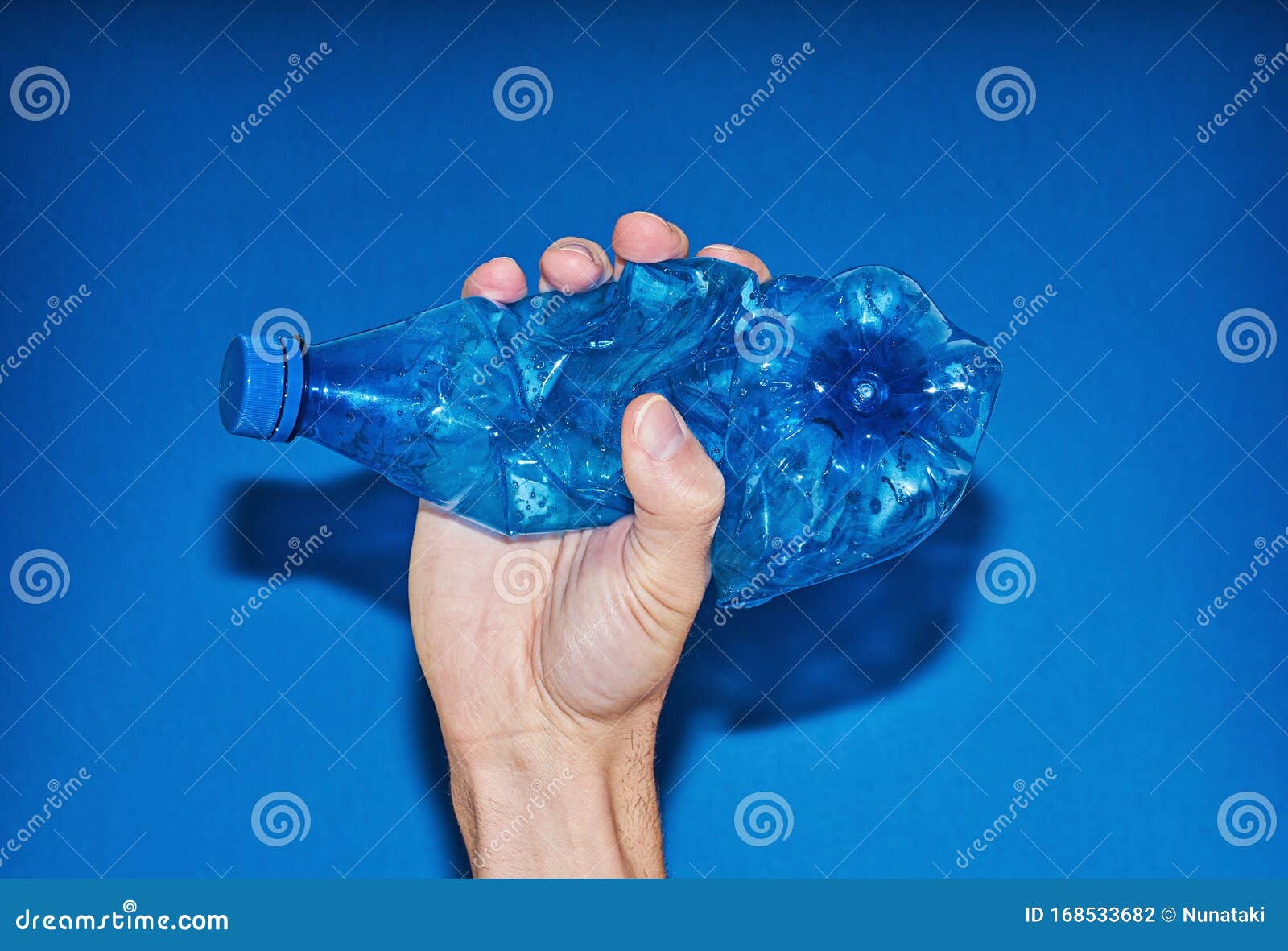 Hand Squeezing Plastic Bottle on Blue Background. Zero Waste Concept