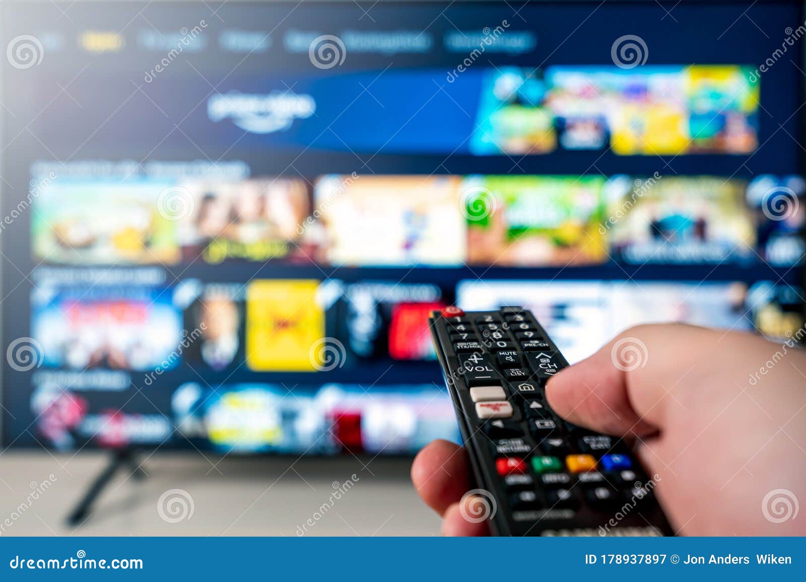 hand with tv remote aimed towards big 4k flat screen oled tv with blurred out tv entertainment system meny.