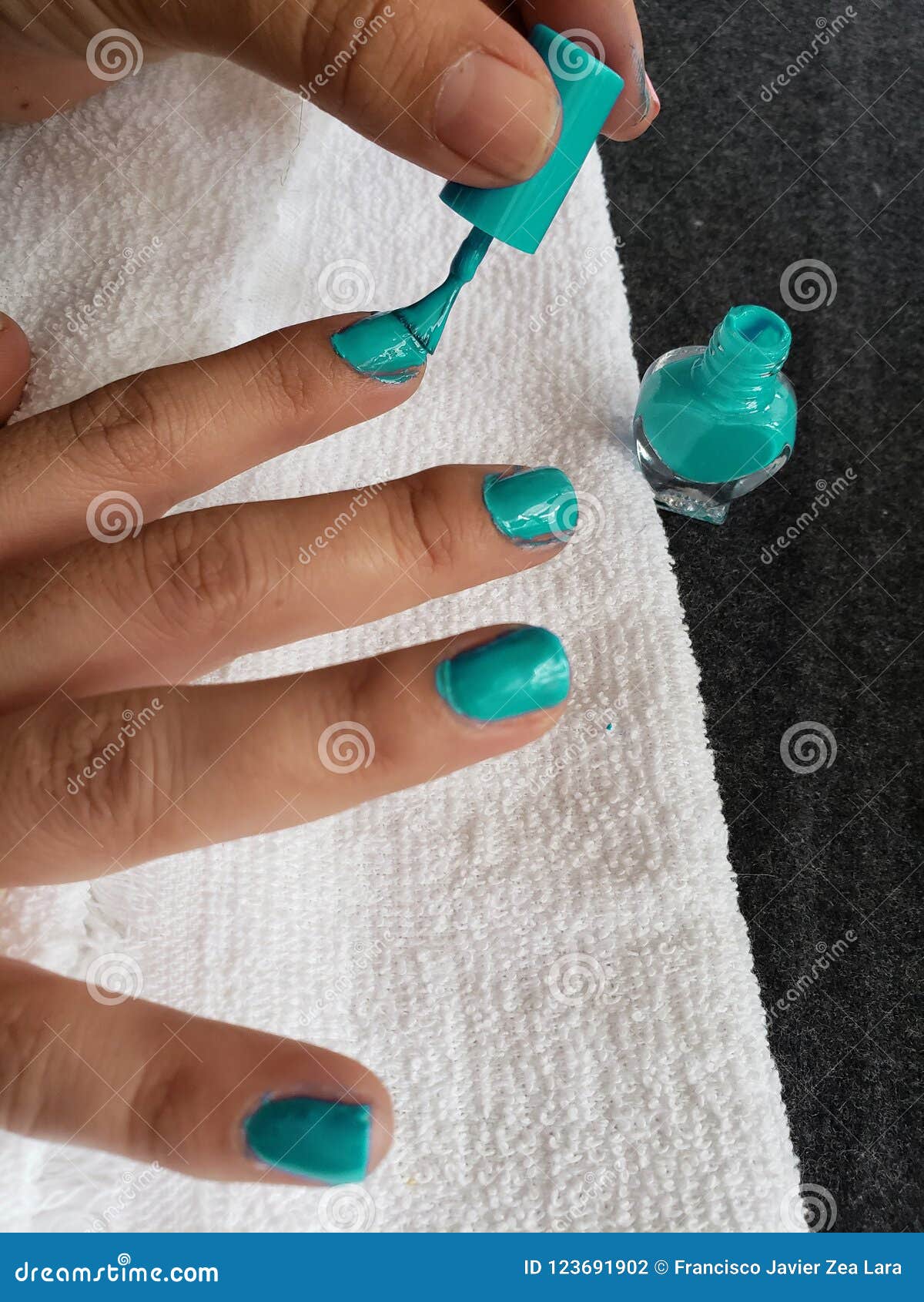 hand of woman painting her nails in aquamarine color
