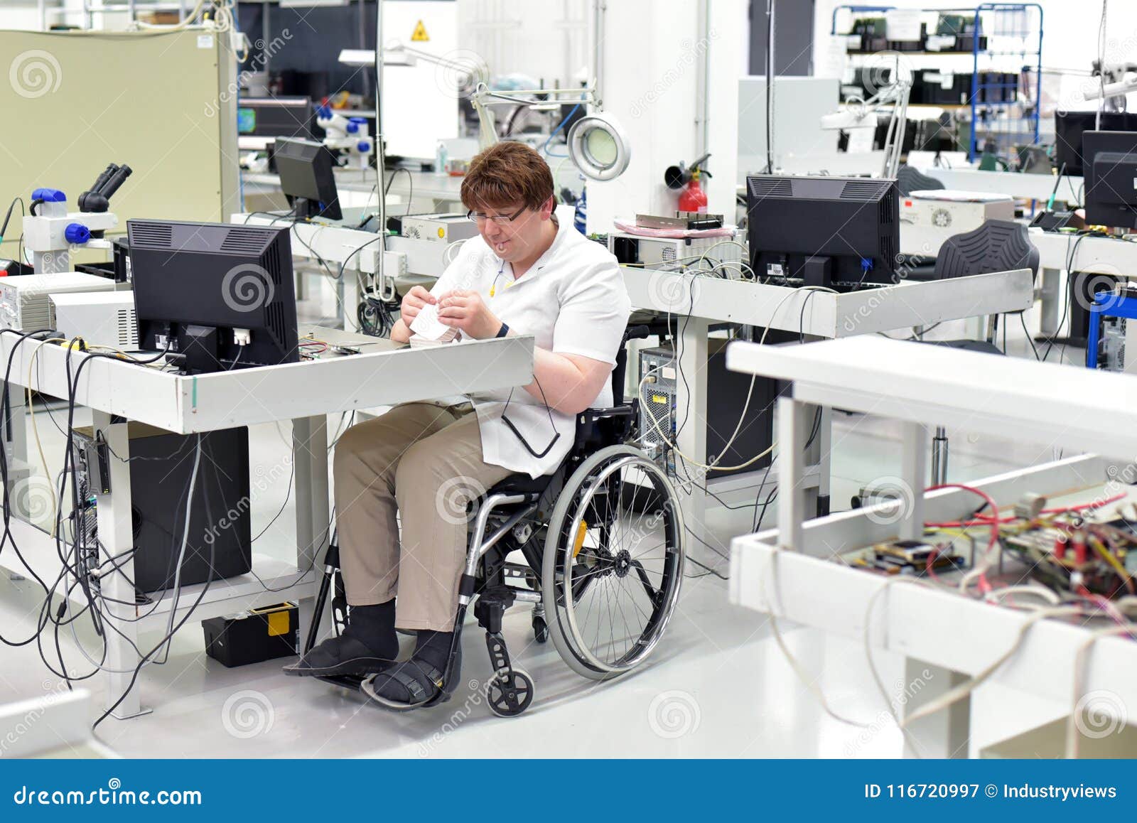 handicapped worker in a wheelchair assembling electronic components in a modern factory at the workplace