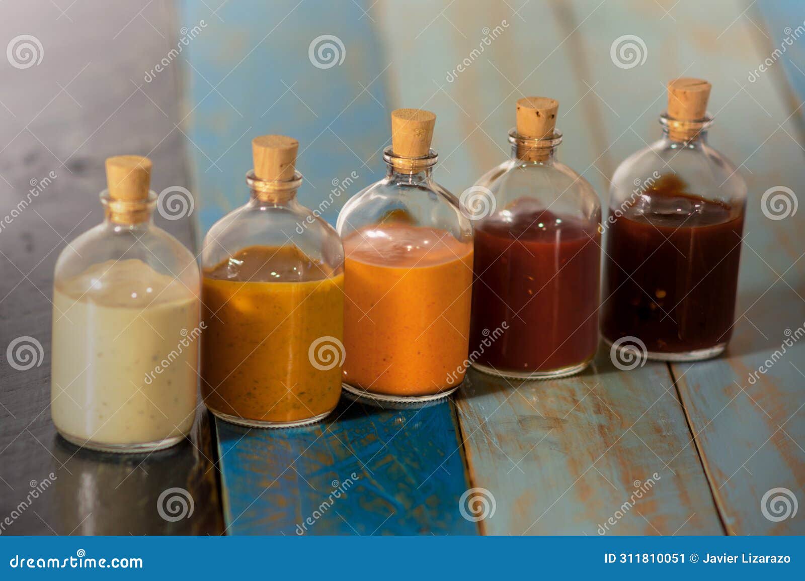handmade spicy sauces in glass bottles with cork on a colored wooden base, salsas picantes hechas artesanalmente en botellas de