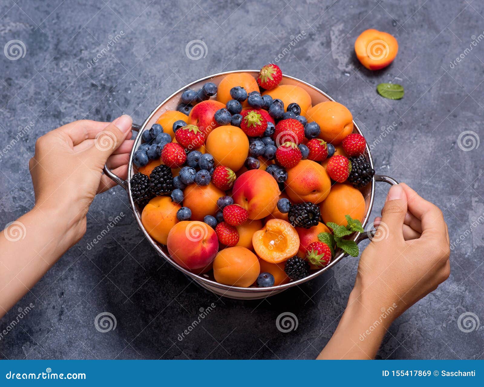 fresh summer fruits and berries, apricots, blueberries, strawberries in colander, woman`s hands holding colander with fruits and