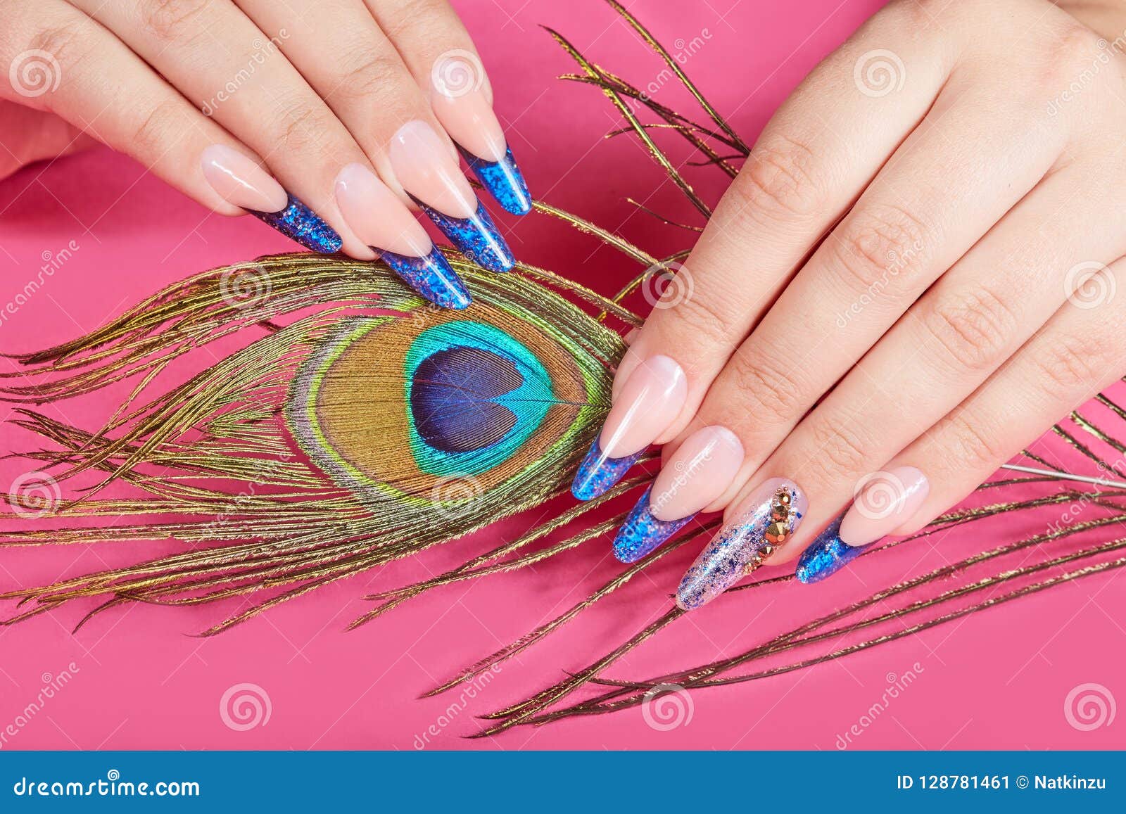 hands with long artificial blue french manicured nails and peacock feather