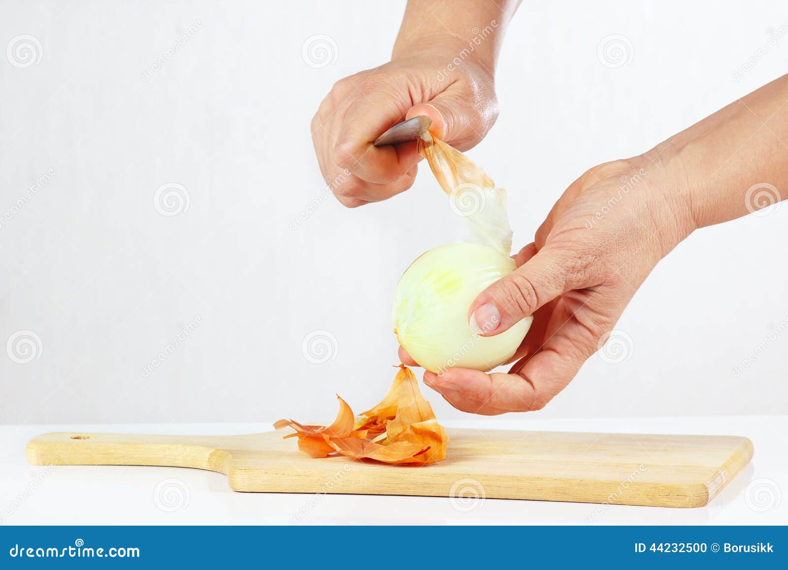 Hands Peeling Raw Onion with a Knife on a Cutting Board Stock Photo