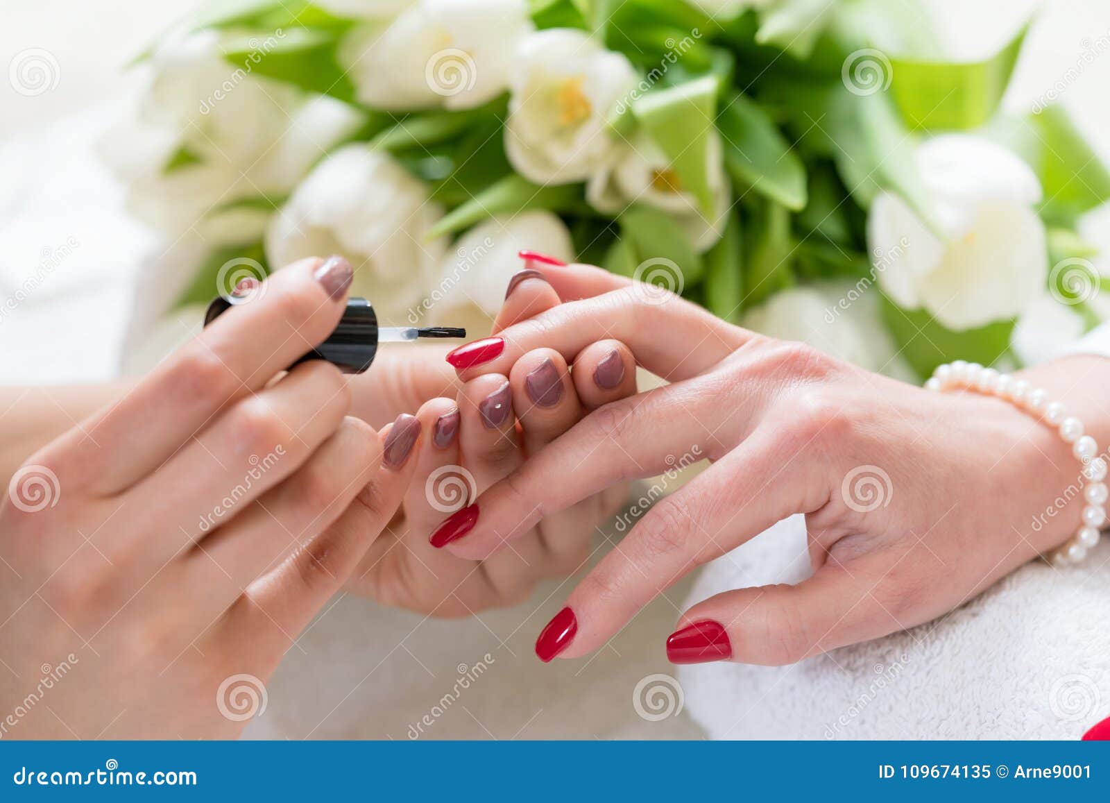 hands of a skilled manicurist applying red nail polish on nails