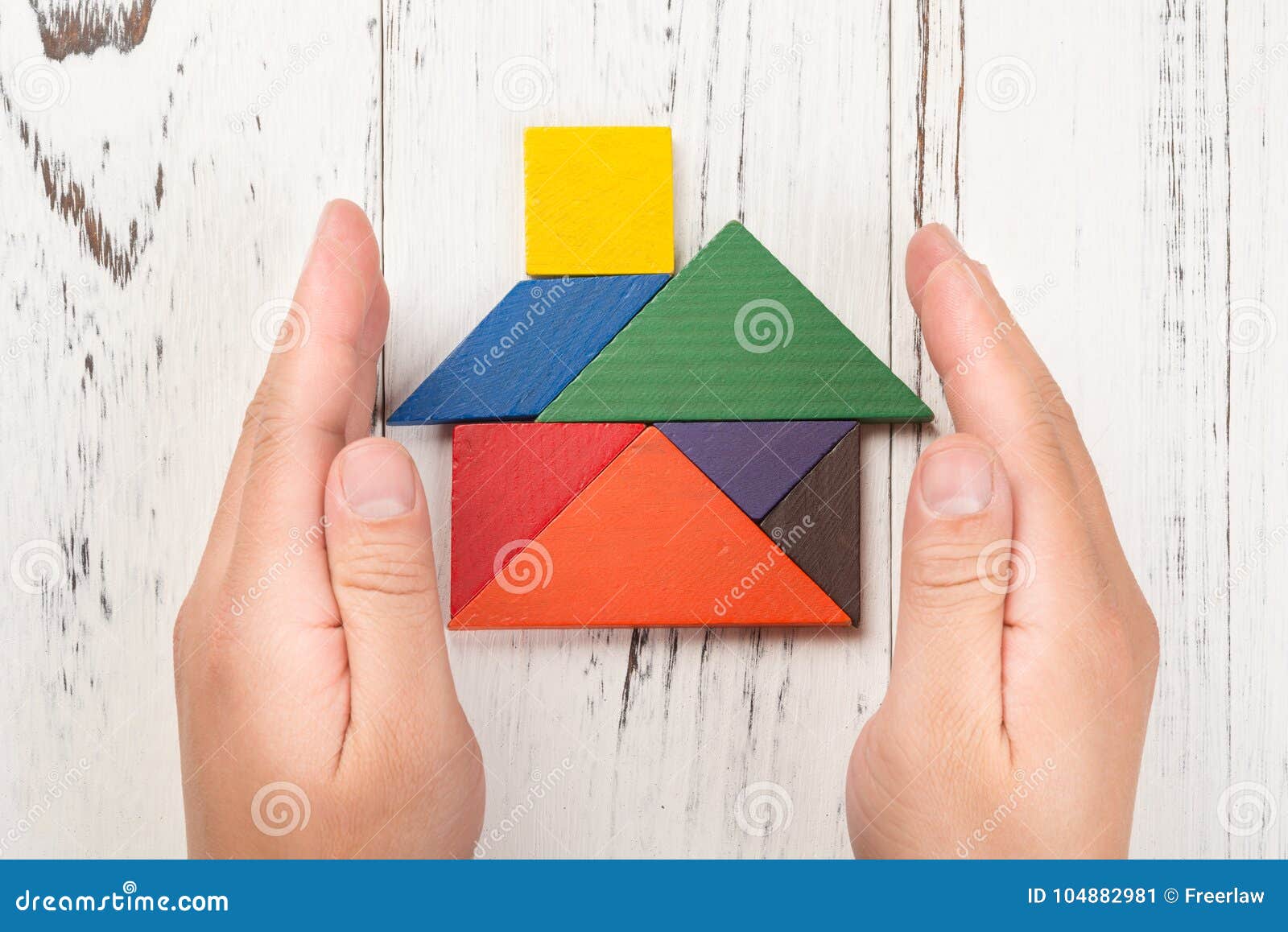 hands surround a wooden house made by tangram home insurance concept and representing home ownership