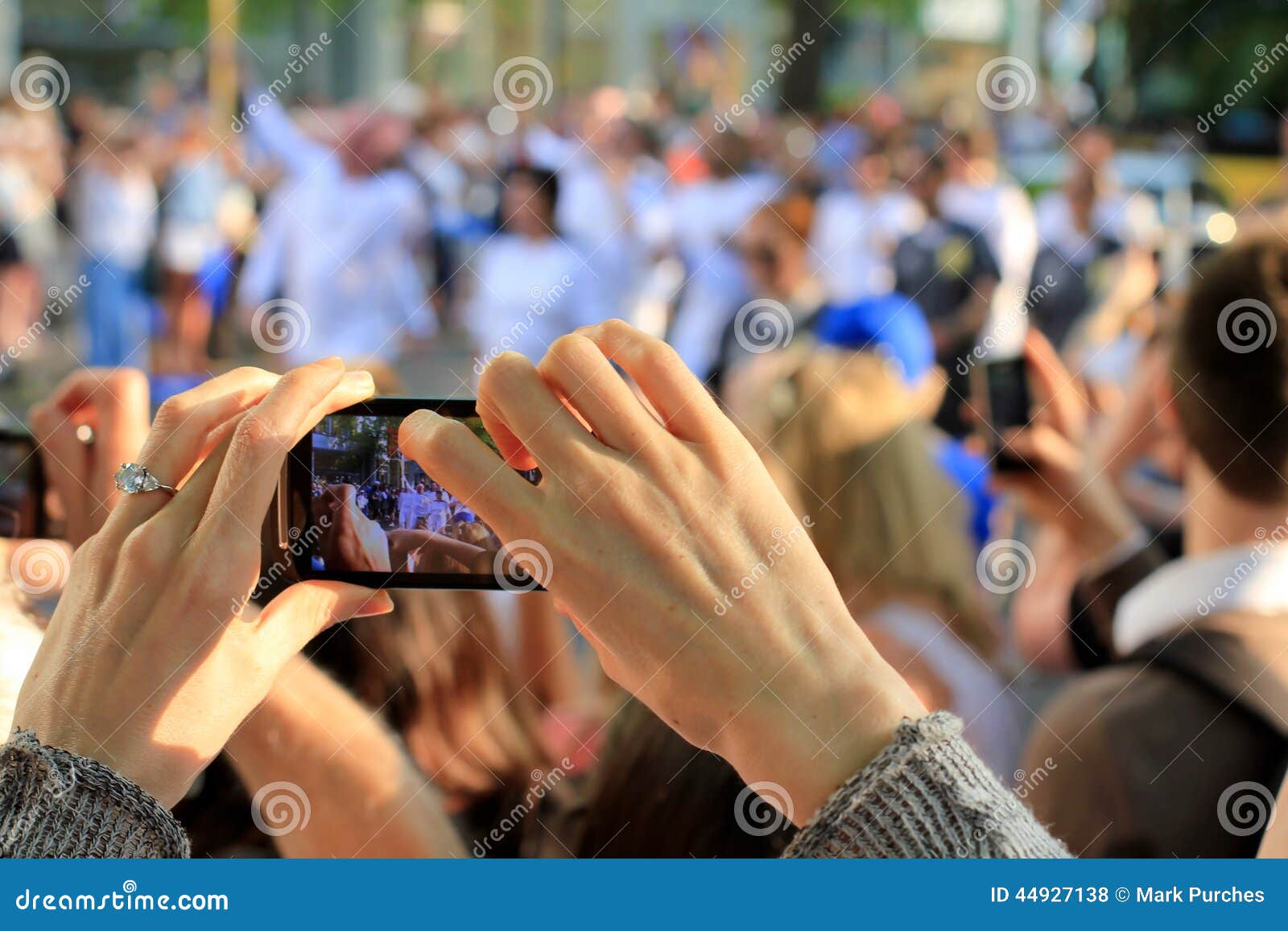 Hands Taking Photo de señora. Las manos de una señora que muestran soportando una cámara elegante del teléfono para tomar una foto de una procesión de la gente para el verano de los Juegos Olímpicos de Londres en 2012 Puede ser utilizado para retratar un evento o una celebración