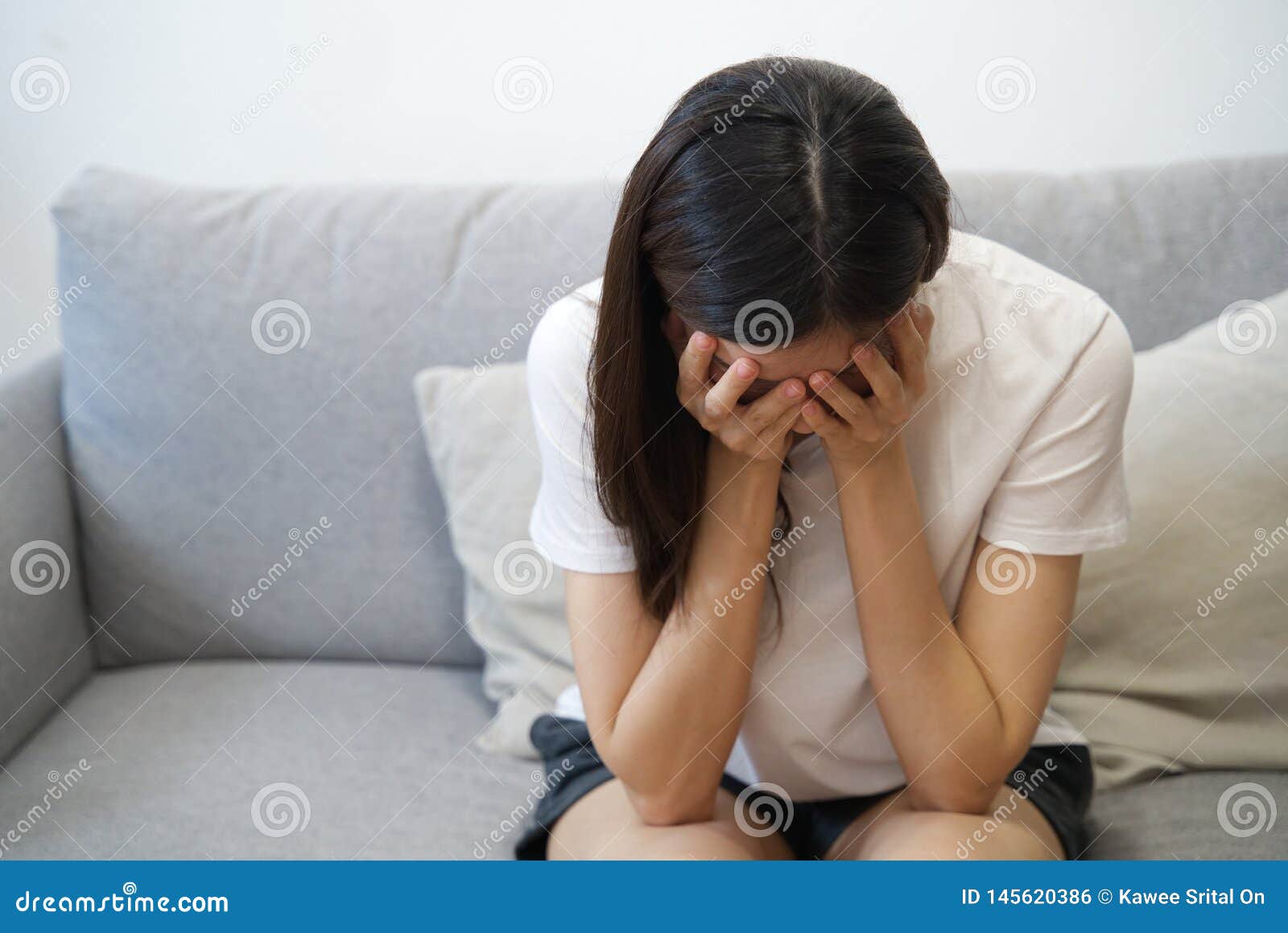 hands on temples of young disappointed  sadness asian girl sitting on sofa. she is feeling not very good due to her sickness and