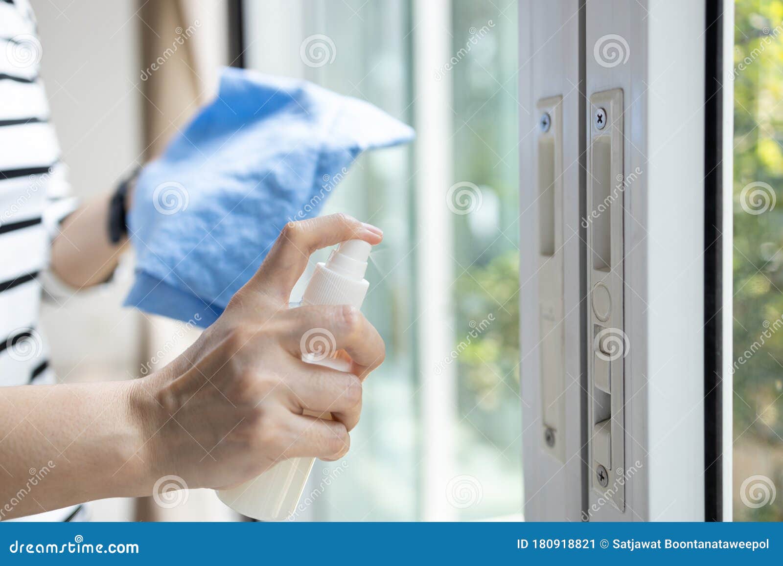 hands of woman with spraying alcohol antiseptic,disinfecting spray,cleaning the front door,sliding glass door handle during the