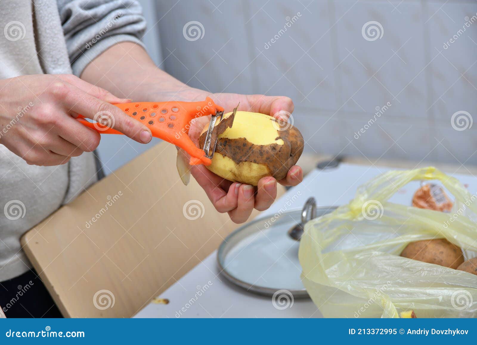 hands of a young woman peeling potatoes with kitchen utensil on a wooden board