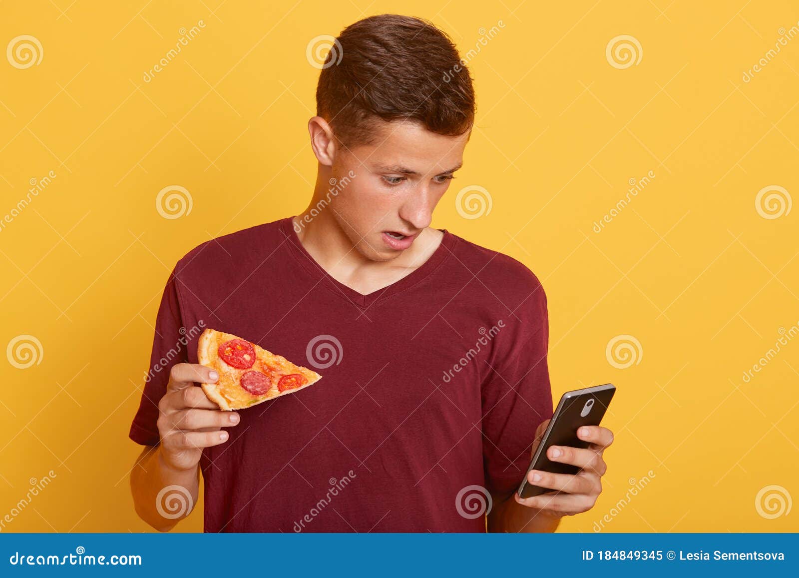 handsome astonish guy holding slice of tasty pizza and phone, checking social network while having snack, sees braking news,