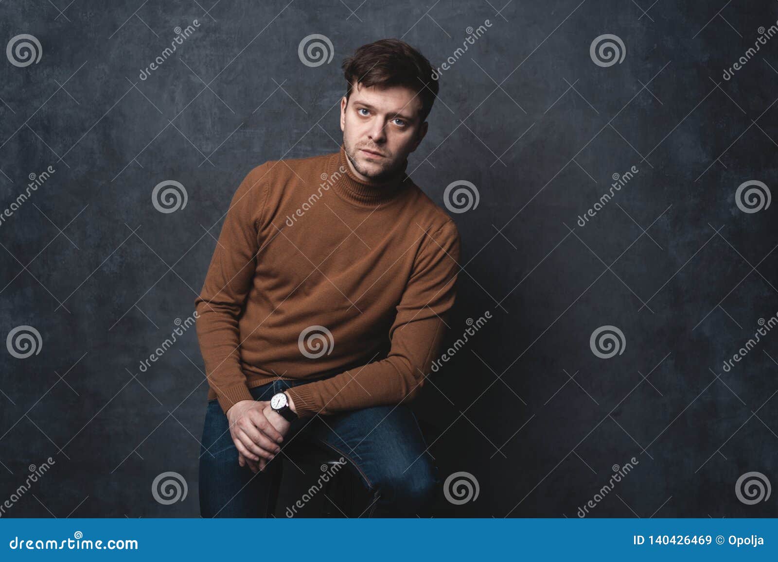 Handsome Casual Man Sits on Chair Near a Dark Gray Wall and Looks To ...
