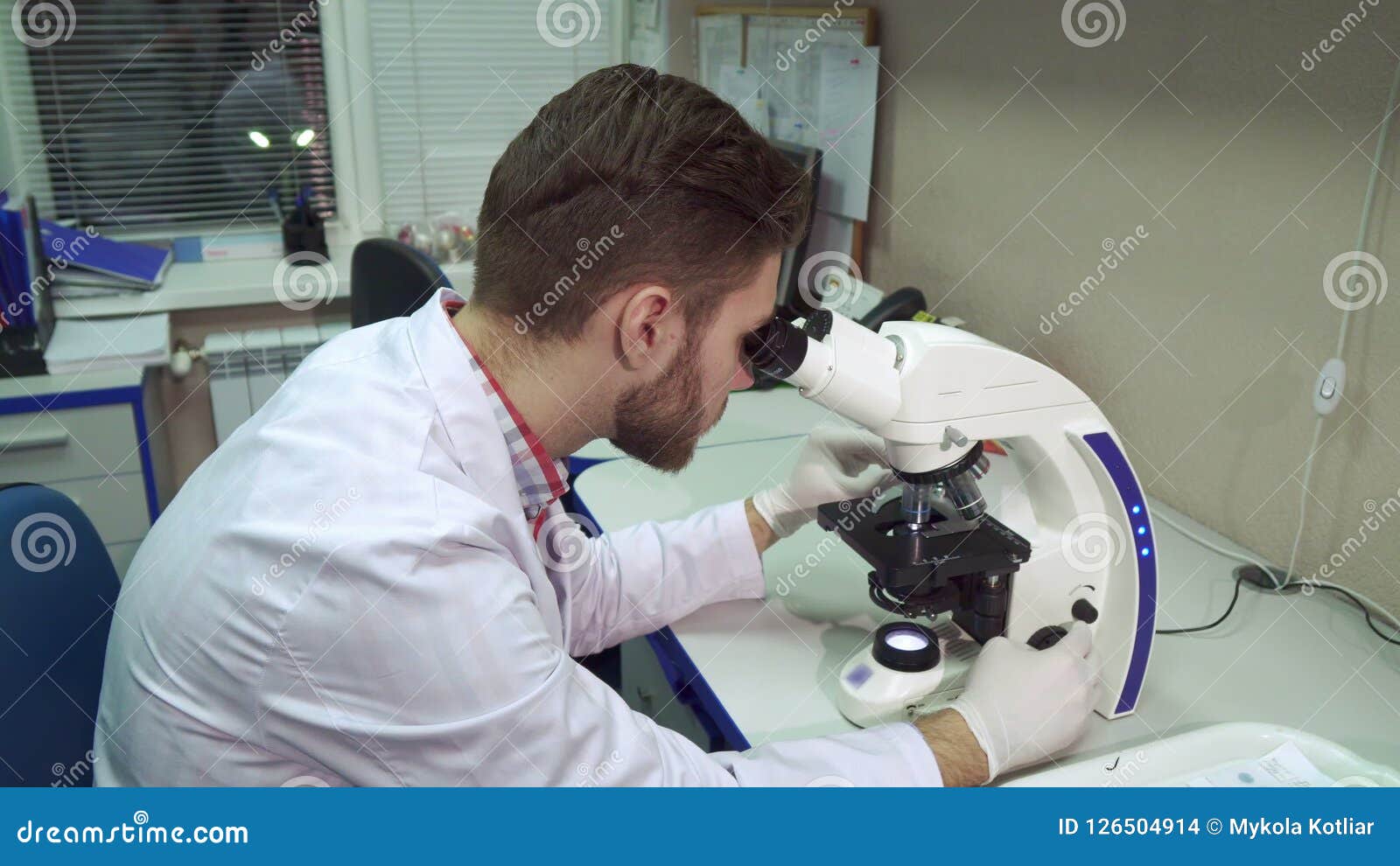 man moves stage clipse on microscope at the laboratory