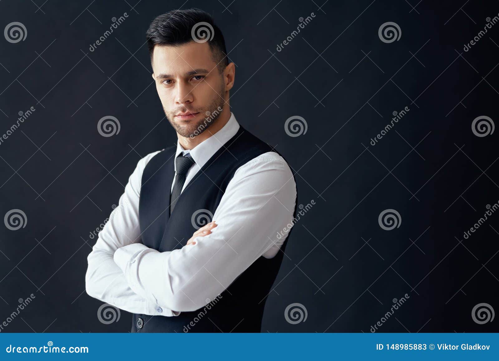 handsome confident man in elegant suit with crossed arms on black background