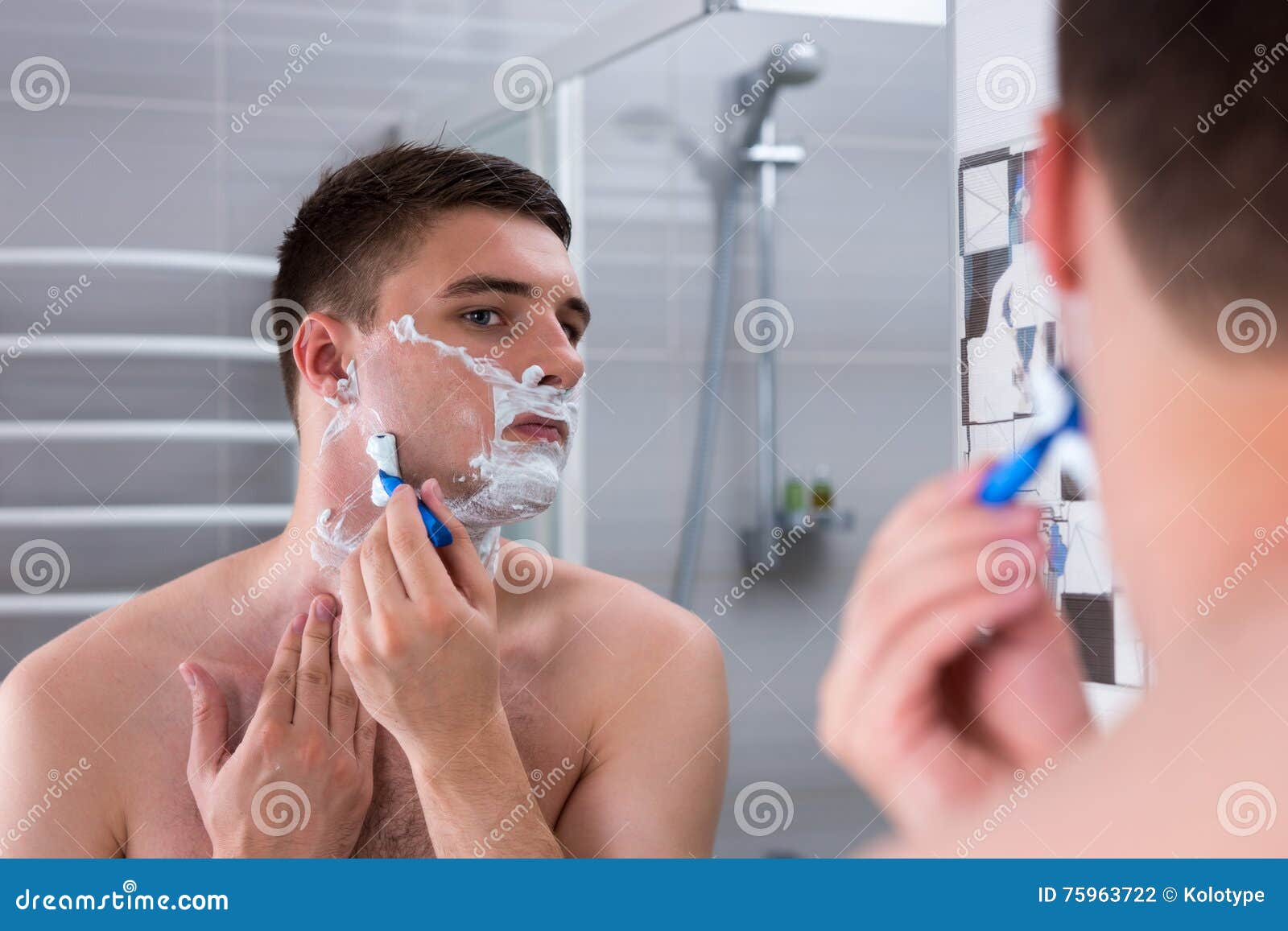 handsome guy shaving his face with a razer and looking at the mi