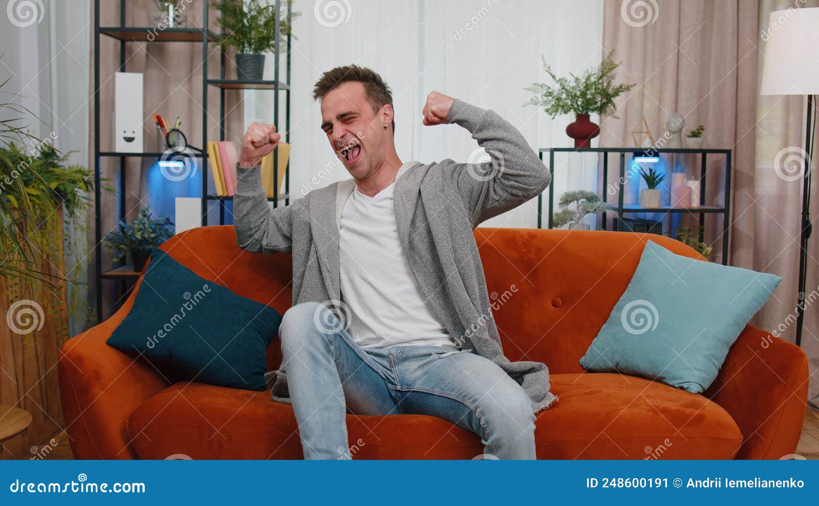 young adult man shouting, receive good news, celebrating success achievemen goal, winning at home