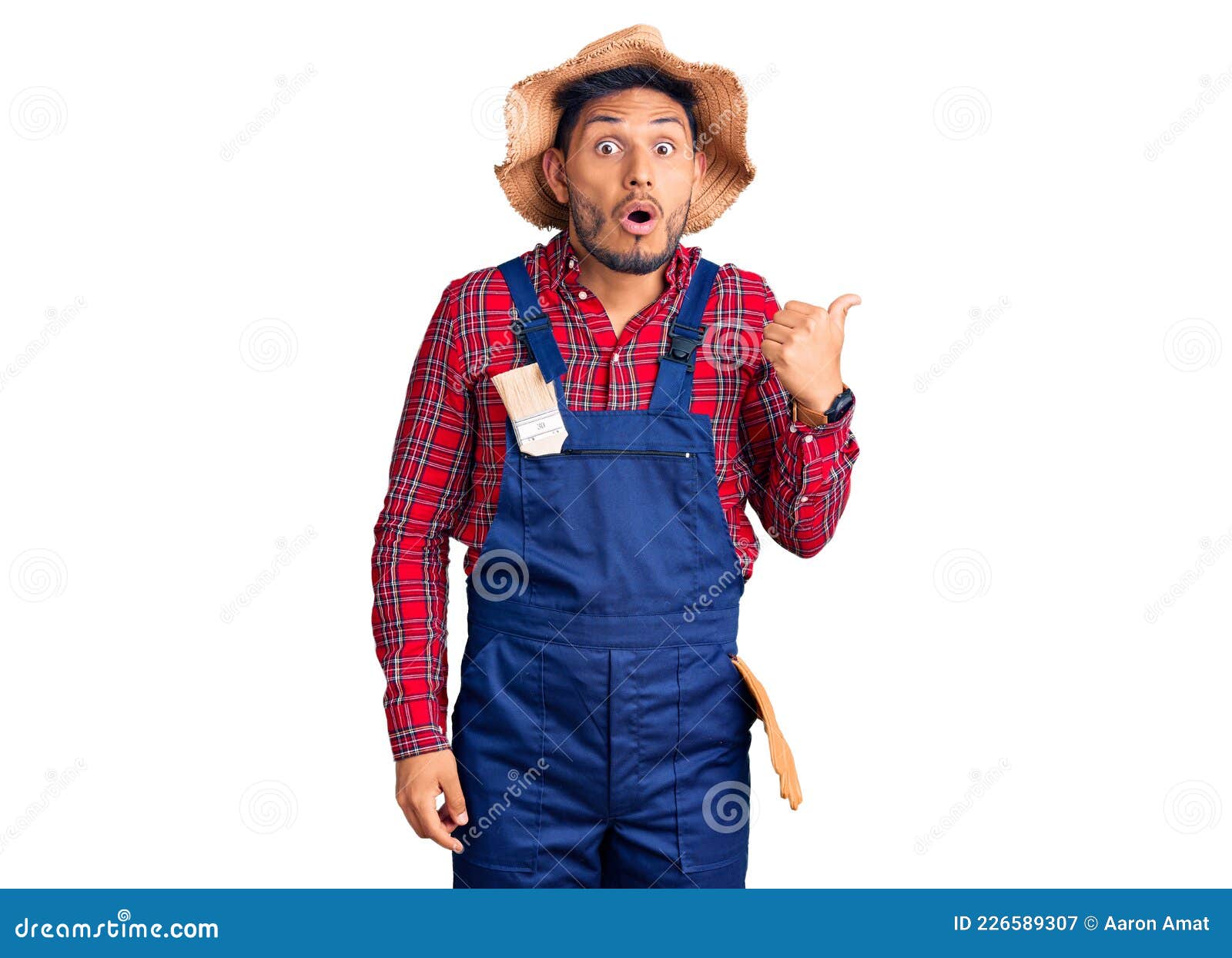 Handsome Latin American Young Man Weaing Handyman Uniform Surprised Pointing With Hand Finger To 