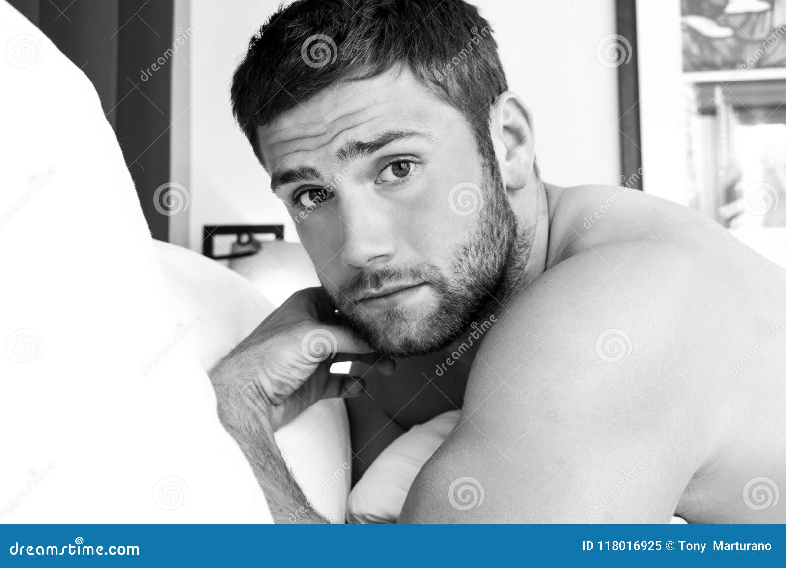 shirtless hunky man with beard lies naked in bed