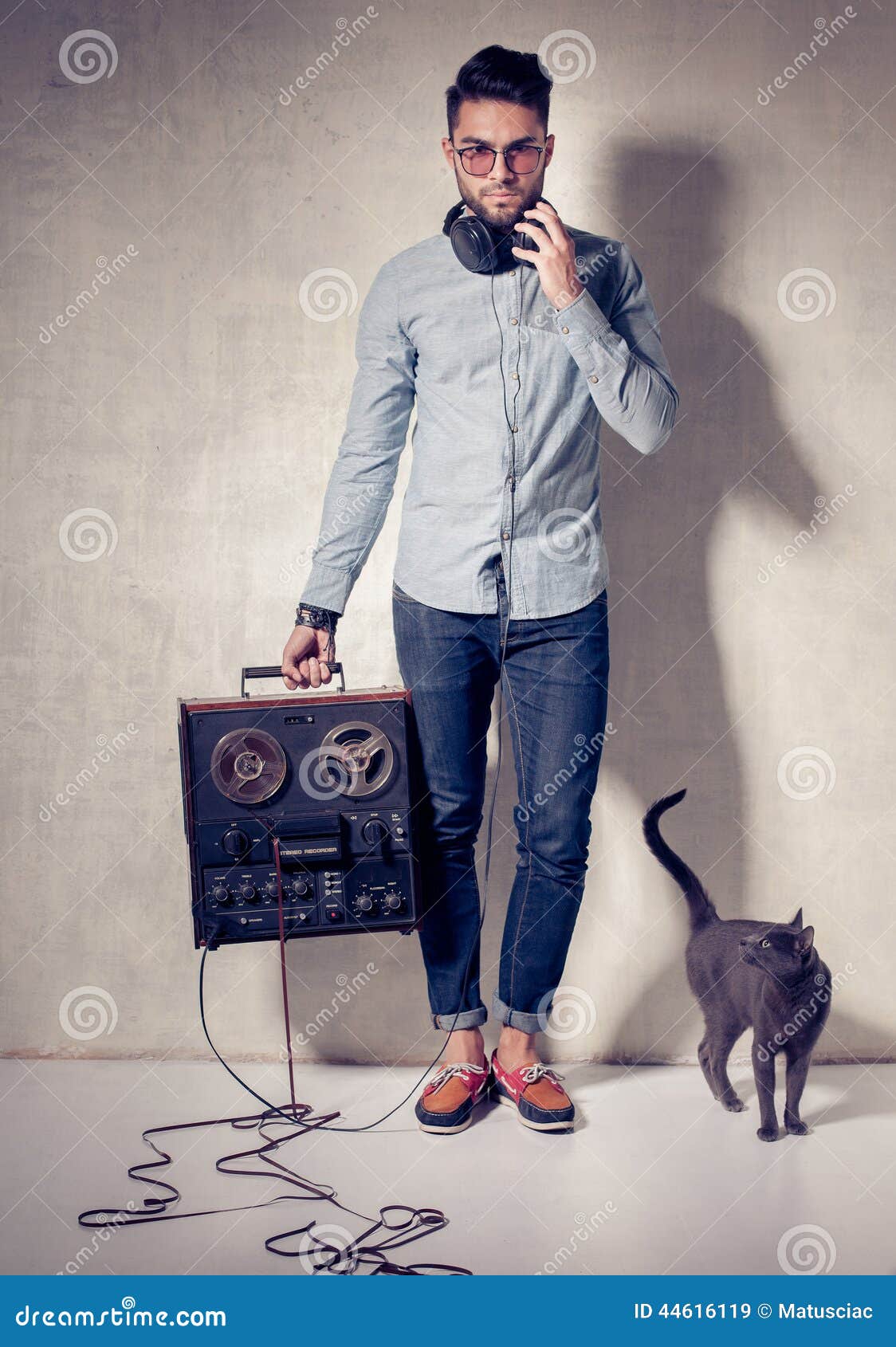 Handsome man and cat listening to music on a magnetophone against grunge wall