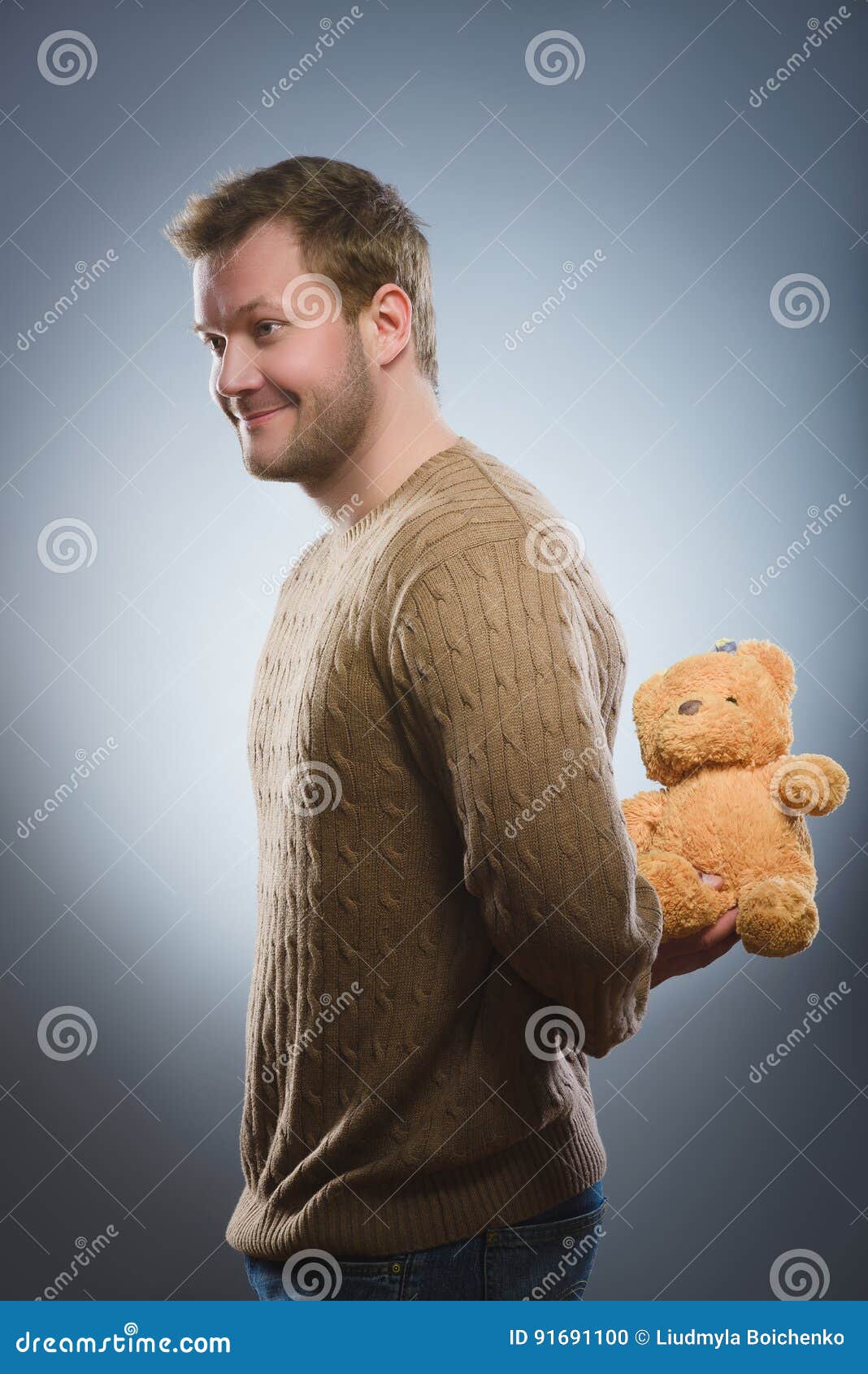 Handsome Man is Holding a Teddy Bear and Smiling on Gray Background