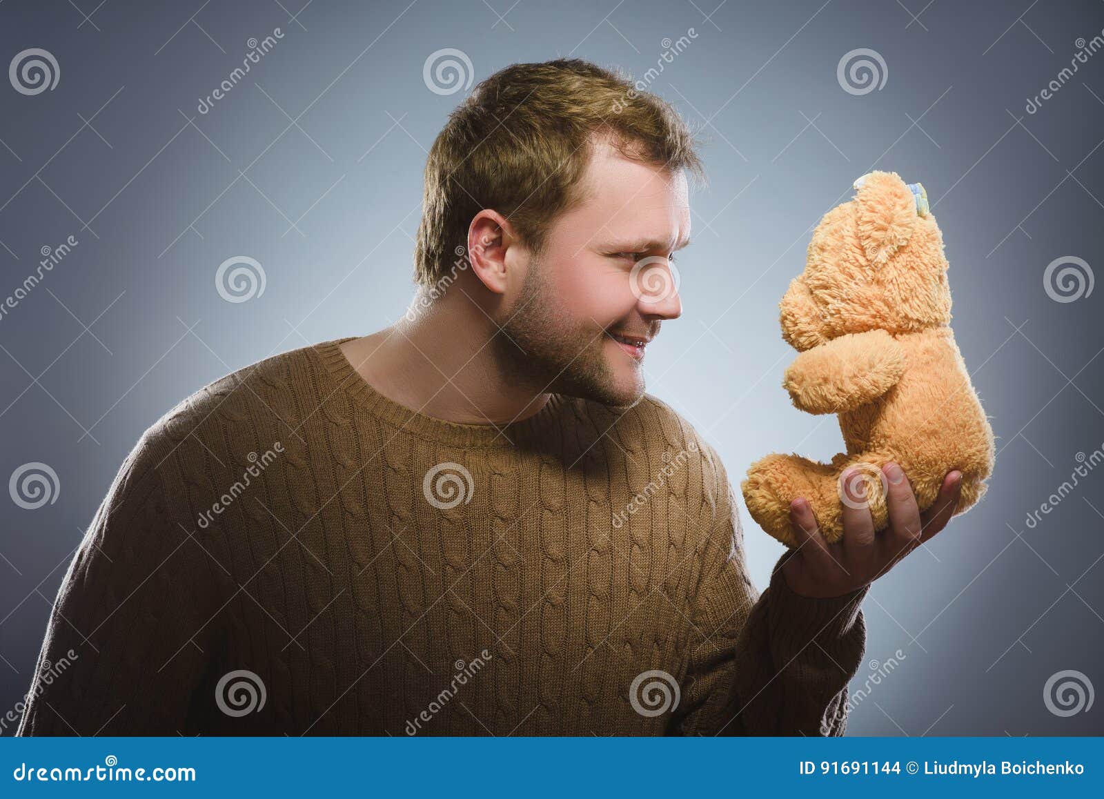Handsome Man is Holding a Teddy Bear and Smiling on Gray Background