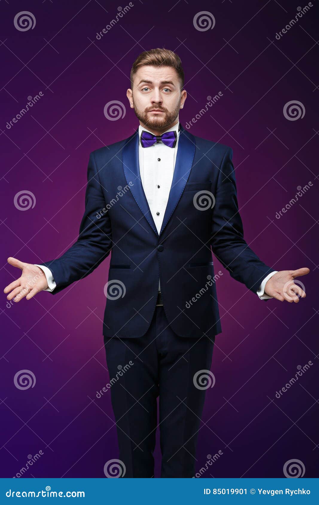 handsome man in tuxedo and bow tie is surprised, throws his hands. compere in fashionable, festive clothing