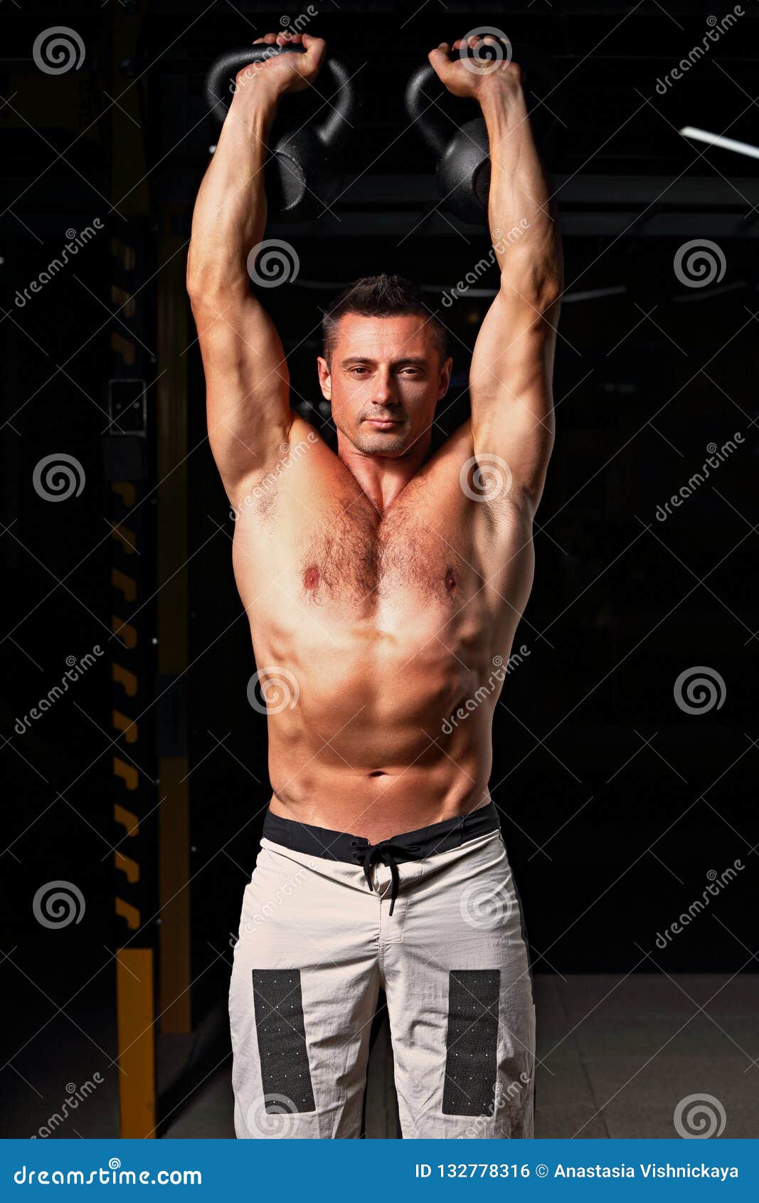 handsome strong man doing the exercises with kettlebells in sportwear shorts on dark shadow background. closeup bright portrait.