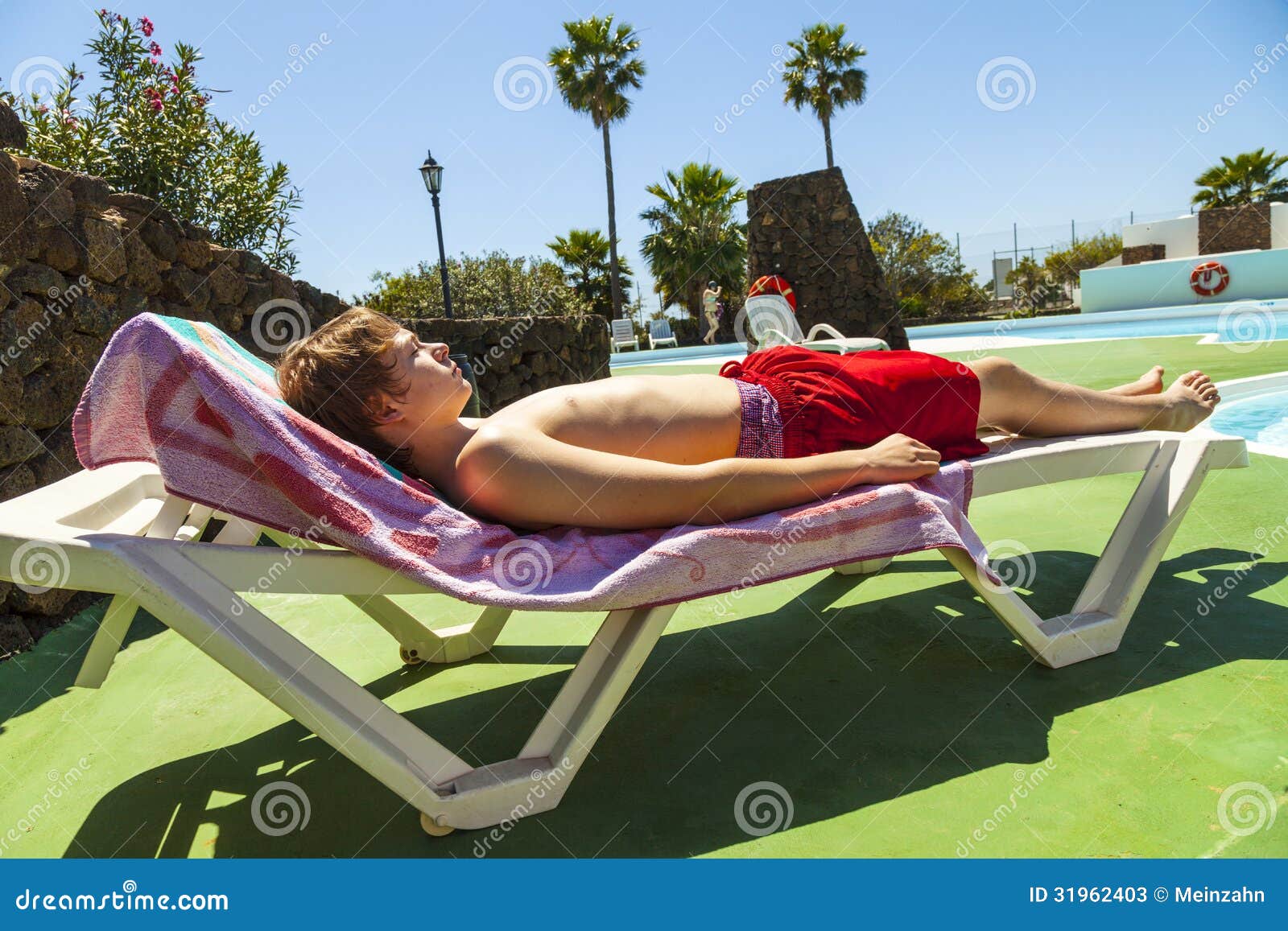 Cute handsome teenage boy rests on a beach couch at the pool