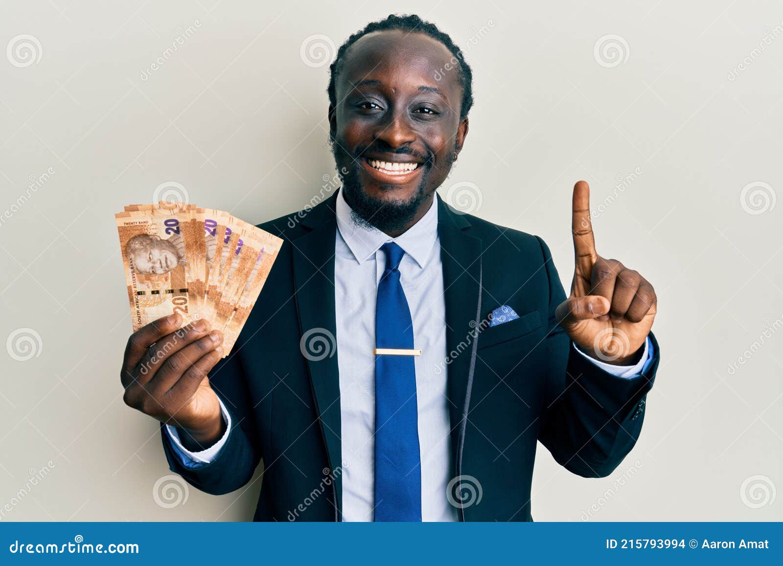 handsome young black man wearing business suit holding 20 rands banknotes smiling with an idea or question pointing finger with