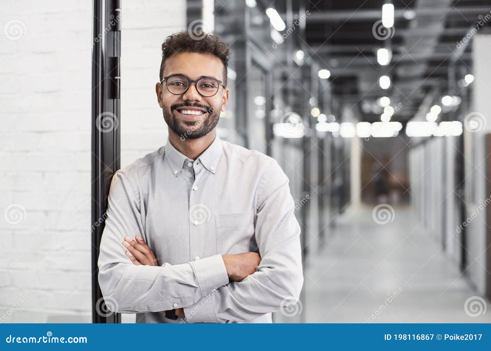 handsome young businessman portrait. cheerful self confident smiling man with crossed hands in office