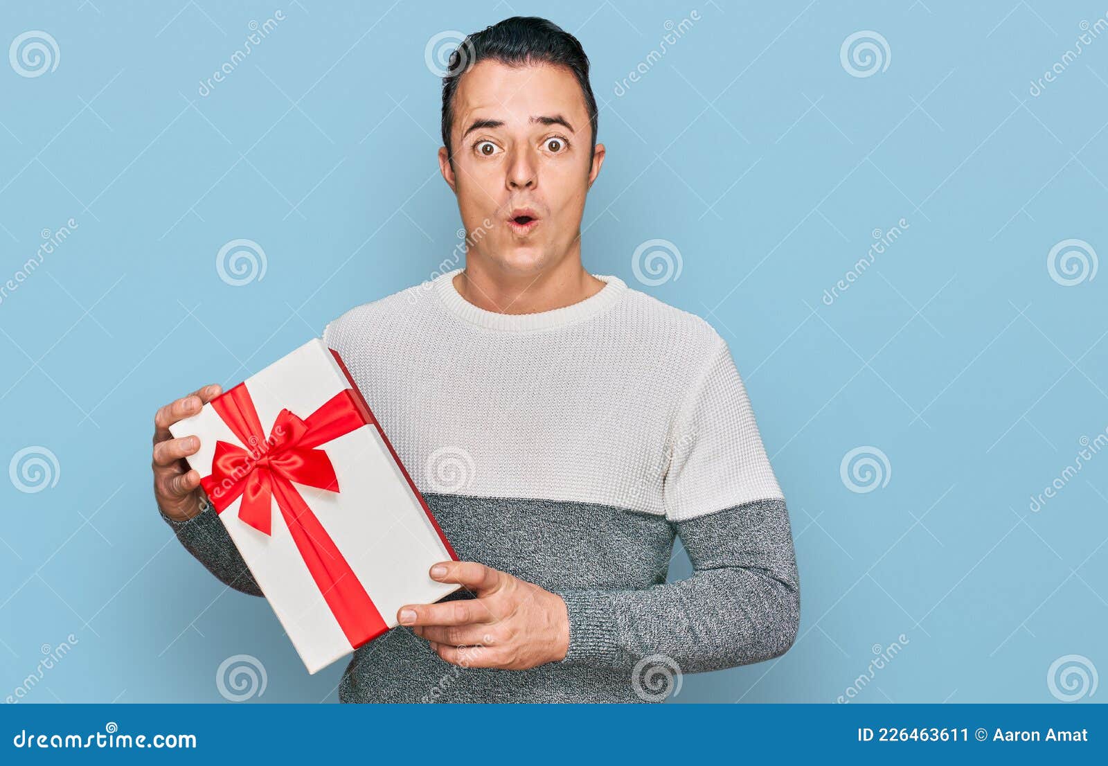 Handsome Young Man Holding Gift Scared and Amazed with Open Mouth for ...