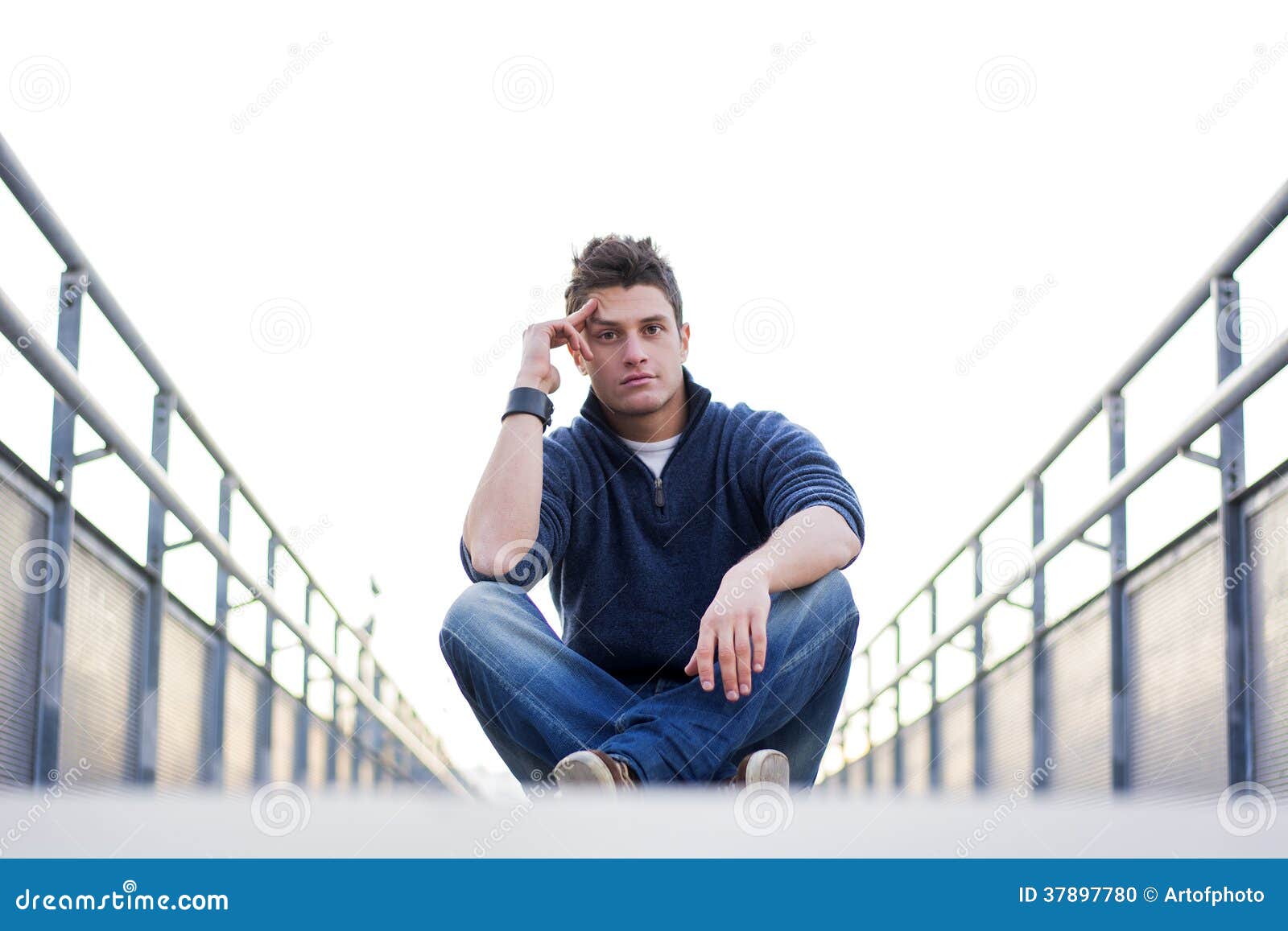 handsome young man sitting between handrails in walkway