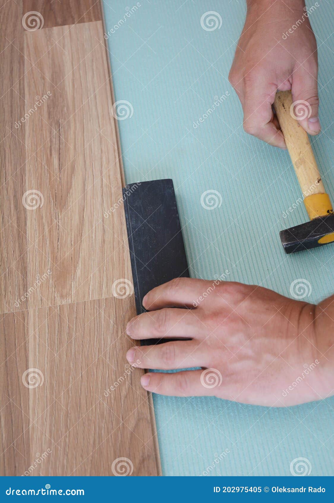 a handyman is installing a wood laminate flooring on the underlayment using a hummer along with a tapping block to snug up the joi