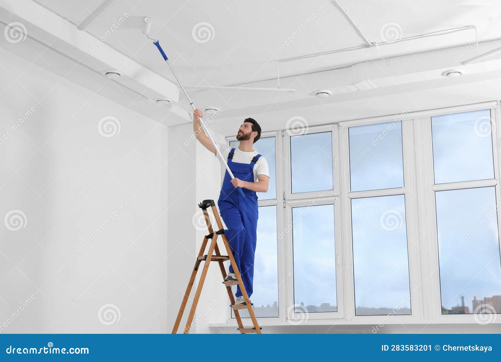 Handyman Painting Ceiling with Roller on Step Ladder in Room Stock