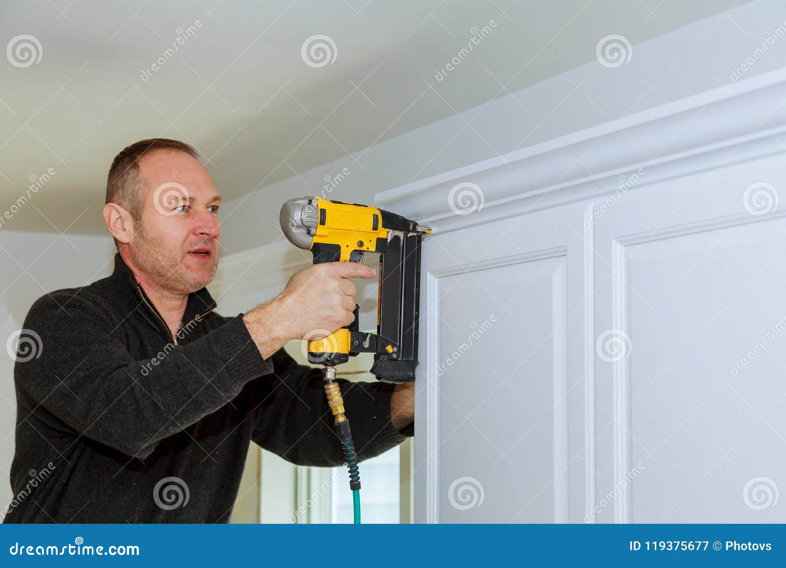 Handyman Working Instal Brad Nail Gun To Crown Moulding Wall